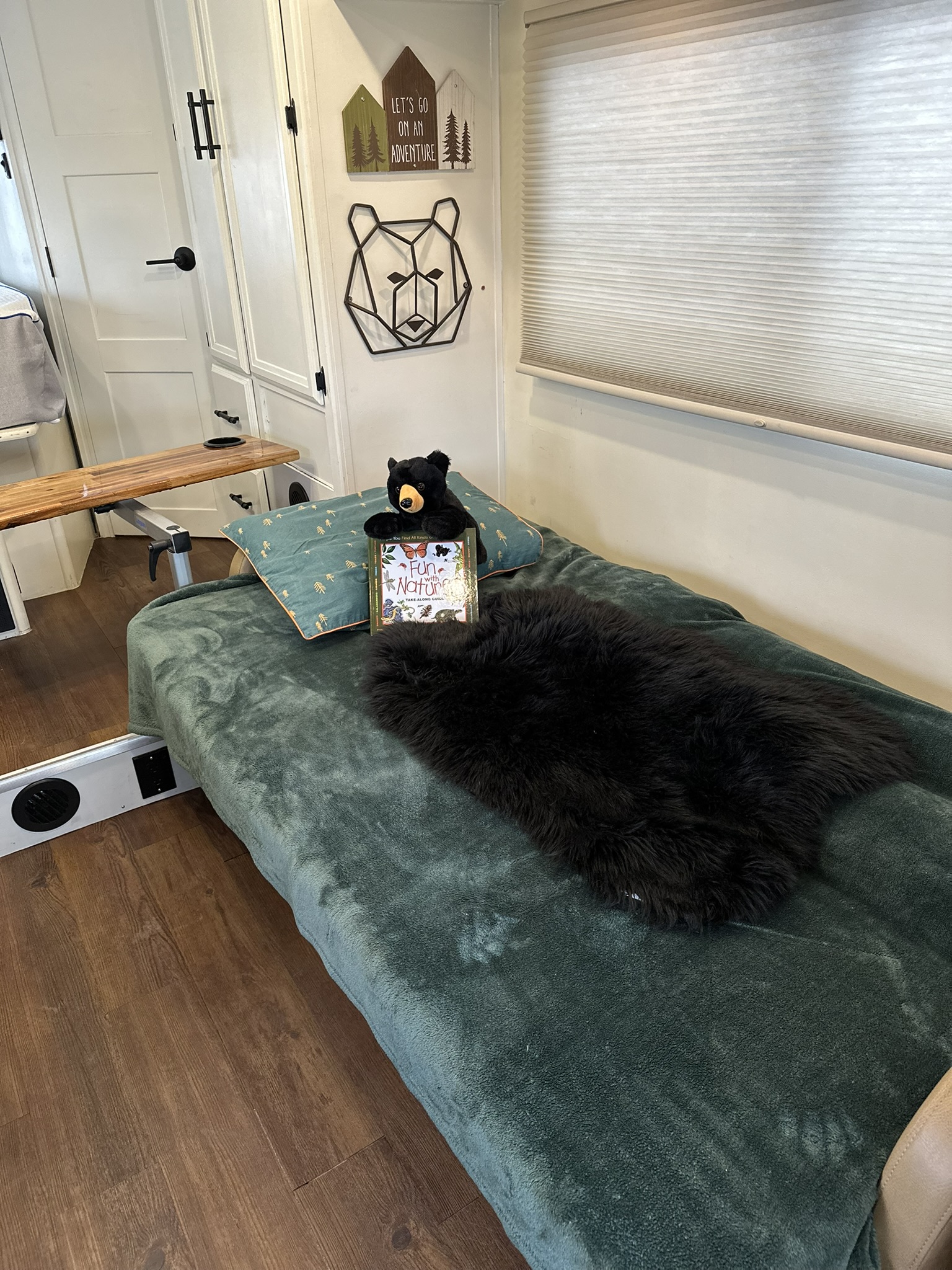 Cozy RV rental interior: a comfy bed with green blanket, plush bear, nature book, and adventure-themed wall decor.. Coachmen Freelander 2019