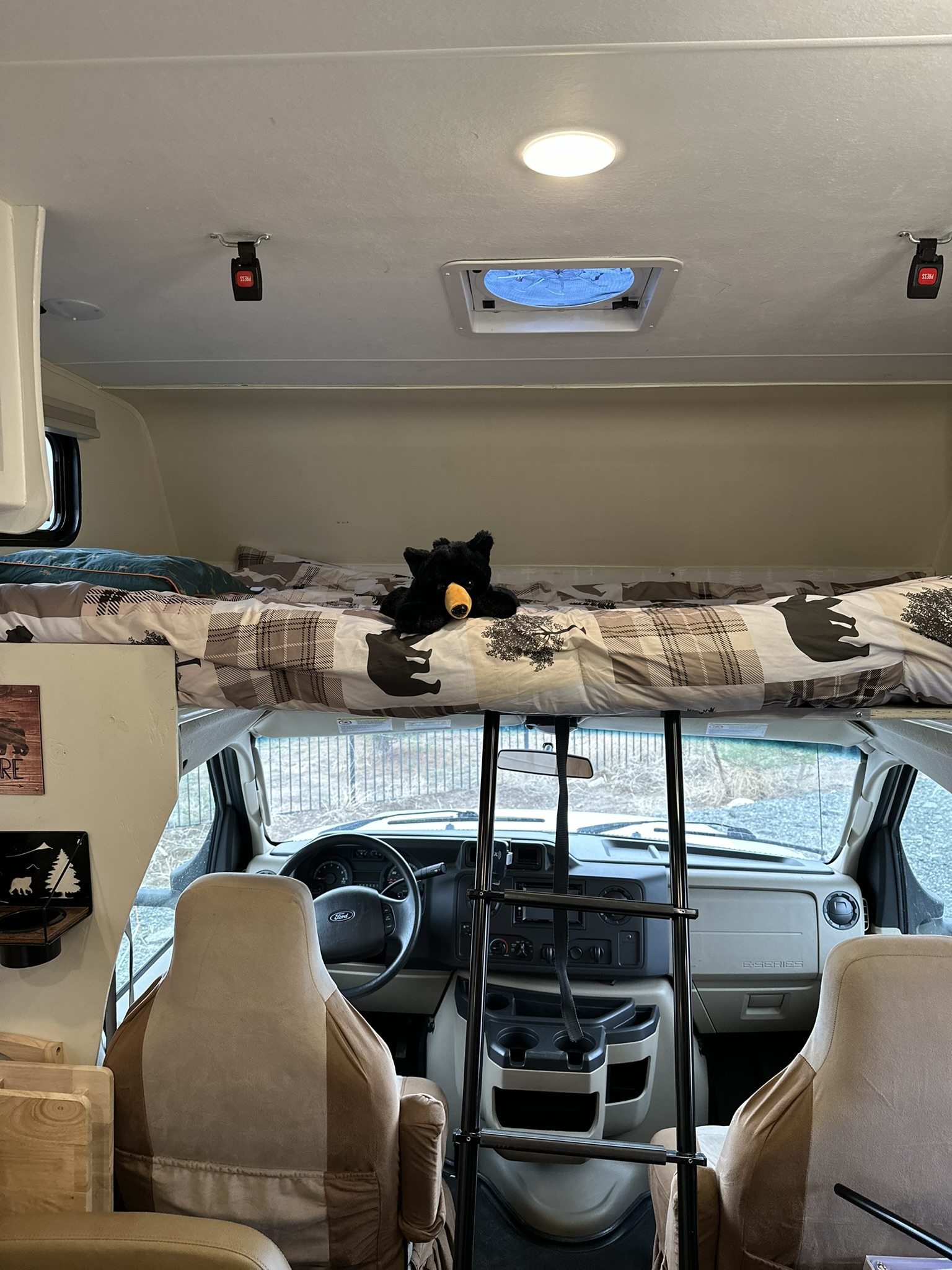 Cozy RV rental interior: overhead bunk with bear bedding, access ladder, and front dashboard. Perfect for road trips.. Coachmen Freelander 2019
