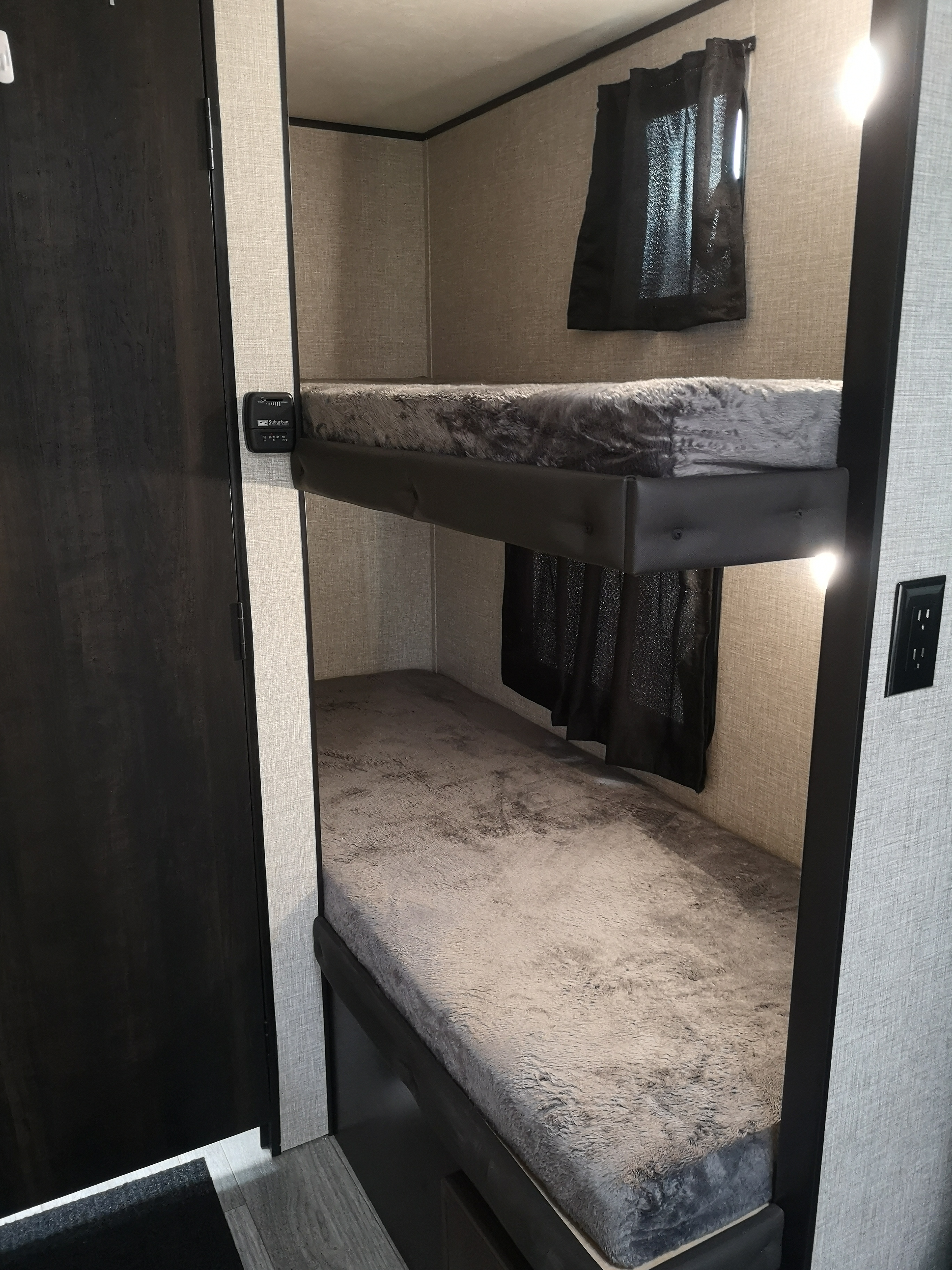 Cozy bunk beds in an RV rental, featuring dark wood and light patterned walls. A thermostat and small window are visible.. Jayco Jay Flight SLX 2022