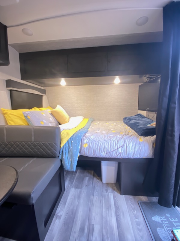 RV rental interior features a bed with colorful bedding, compact seating, overhead storage, and a mounted TV.. Highland Ridge RV Range Lite 2022