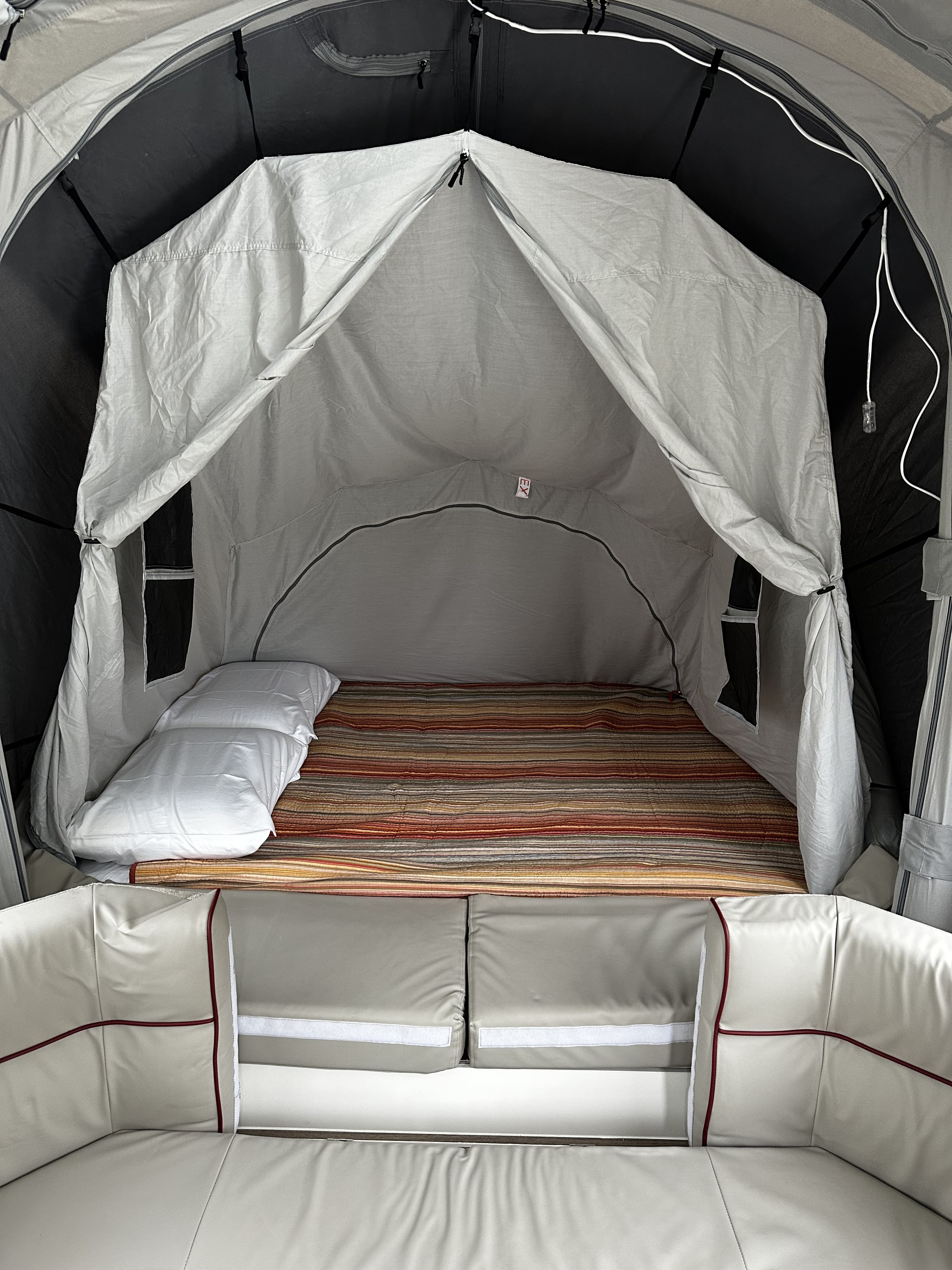 RV rental interior: a light grey tented sleeping area with a striped bed, white pillows, and cream vehicle seating.. Other Other 2022