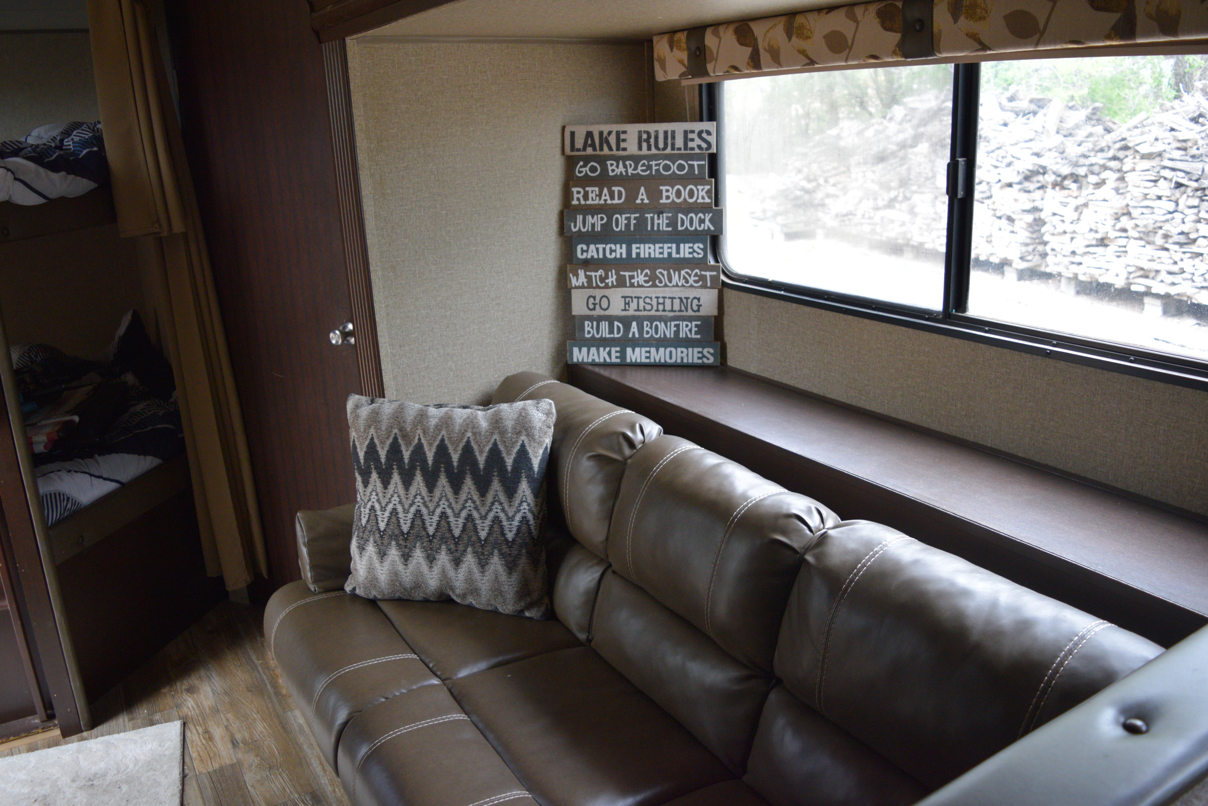 Cozy RV rental interior: brown couch with chevron pillow, bunk beds, and a window with a view. "Lake Rules" sign adds charm.. Forest River Cherokee 2017