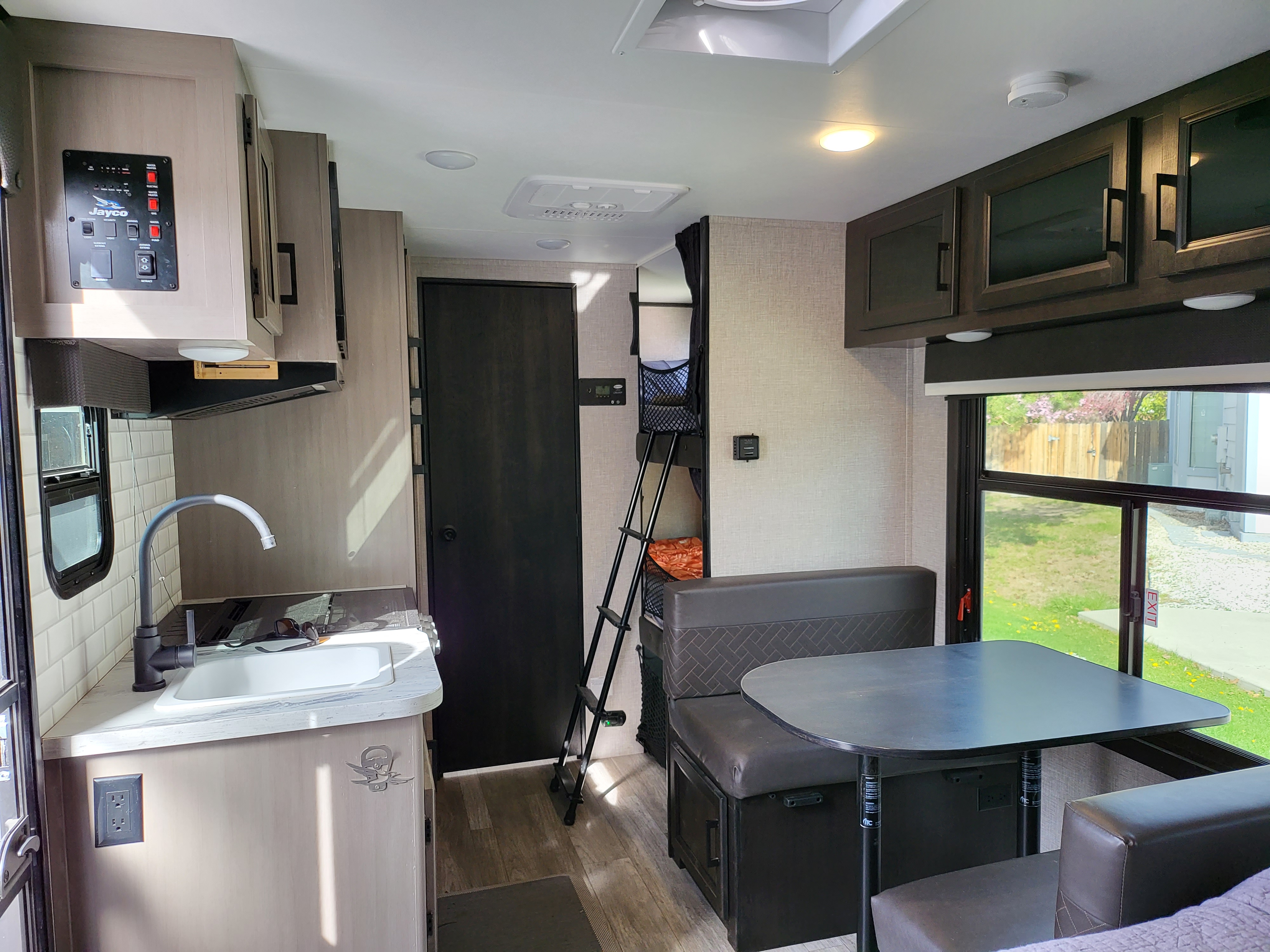 View inside an RV rental, showing a compact kitchen, dinette, bunk beds with ladder, and control panel. Functional layout.. Jayco Jay Feather Micro 2022
