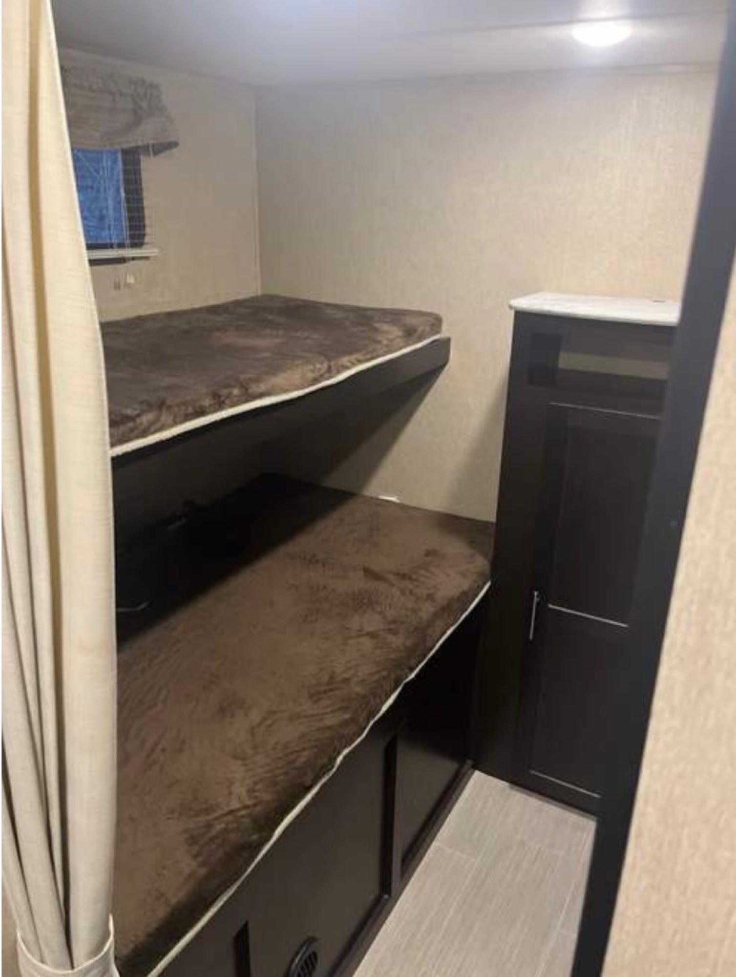 Cozy RV rental sleeping area featuring two bunk beds with plush brown covers, a window, and storage cabinet.. Dutchmen Kodiak Express 2018