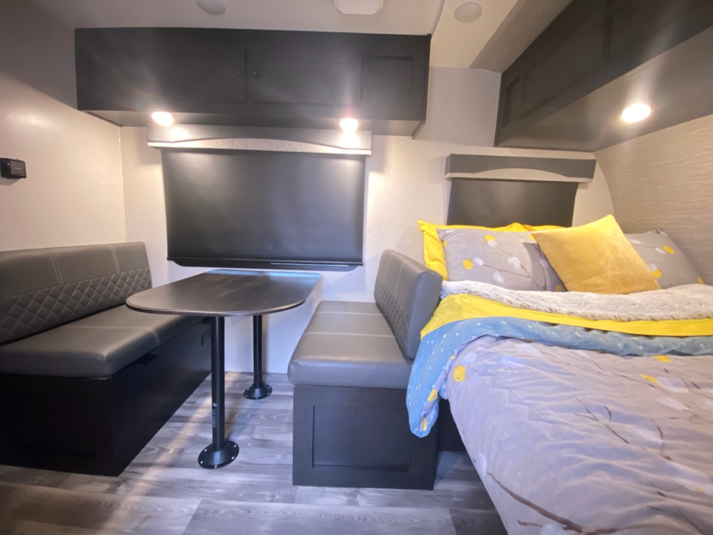 Cozy RV rental interior: dining booth, table, and comfy bed with yellow pillows. Perfect for your next road trip adventure.. Highland Ridge RV Range Lite 2022