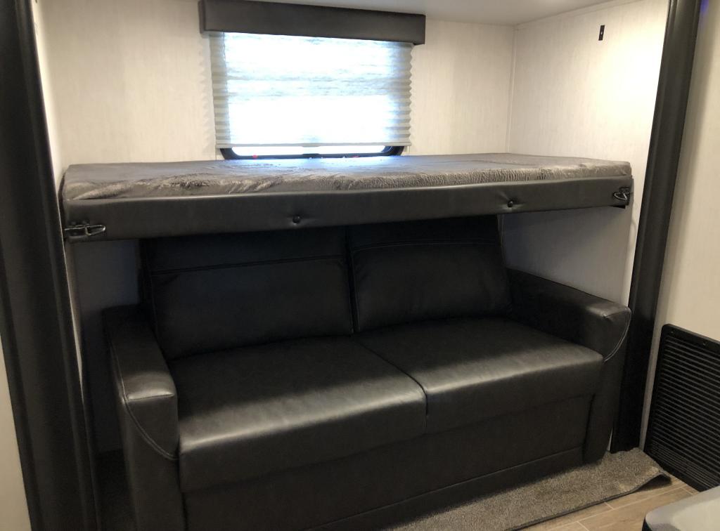 RV rental interior: black faux leather sofa below a fold-down bunk bed, offering versatile seating and sleeping.. Forest River Cherokee Arctic Wolf 2022