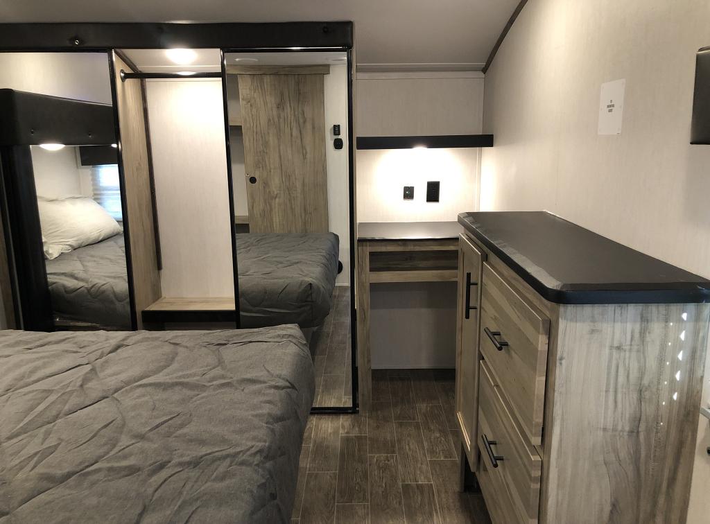 RV rental bedroom interior with a gray bed, mirrored closet, built-in desk, and wood-toned storage.. Forest River Cherokee Arctic Wolf 2022