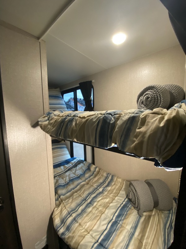 Inside an RV rental: cozy bunk beds with blue/beige striped bedding & rolled grey blankets, a mountain view from the window.. Highland Ridge RV Range Lite 2022
