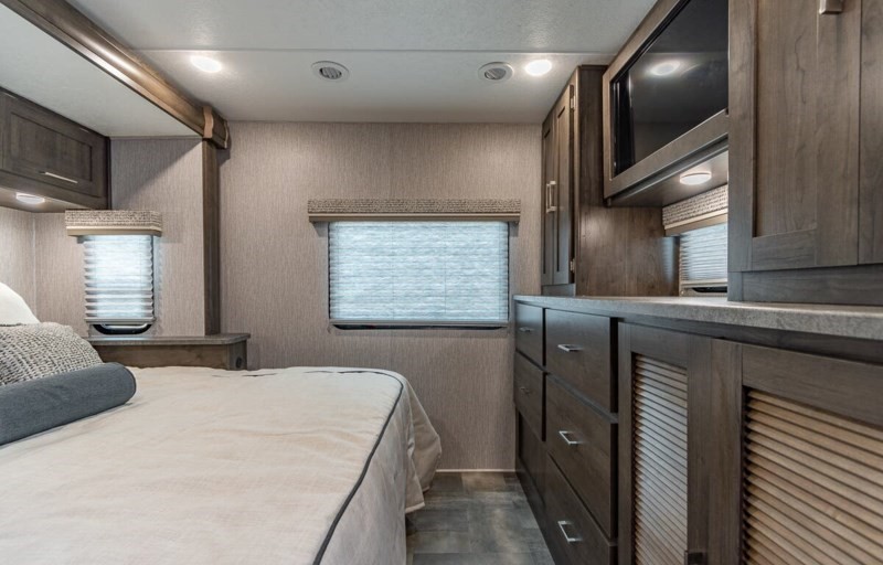 Modern RV rental bedroom interior features a bed, windows, and built-in cabinetry for comfortable travel accommodation.. Coachmen Pursuit 2022