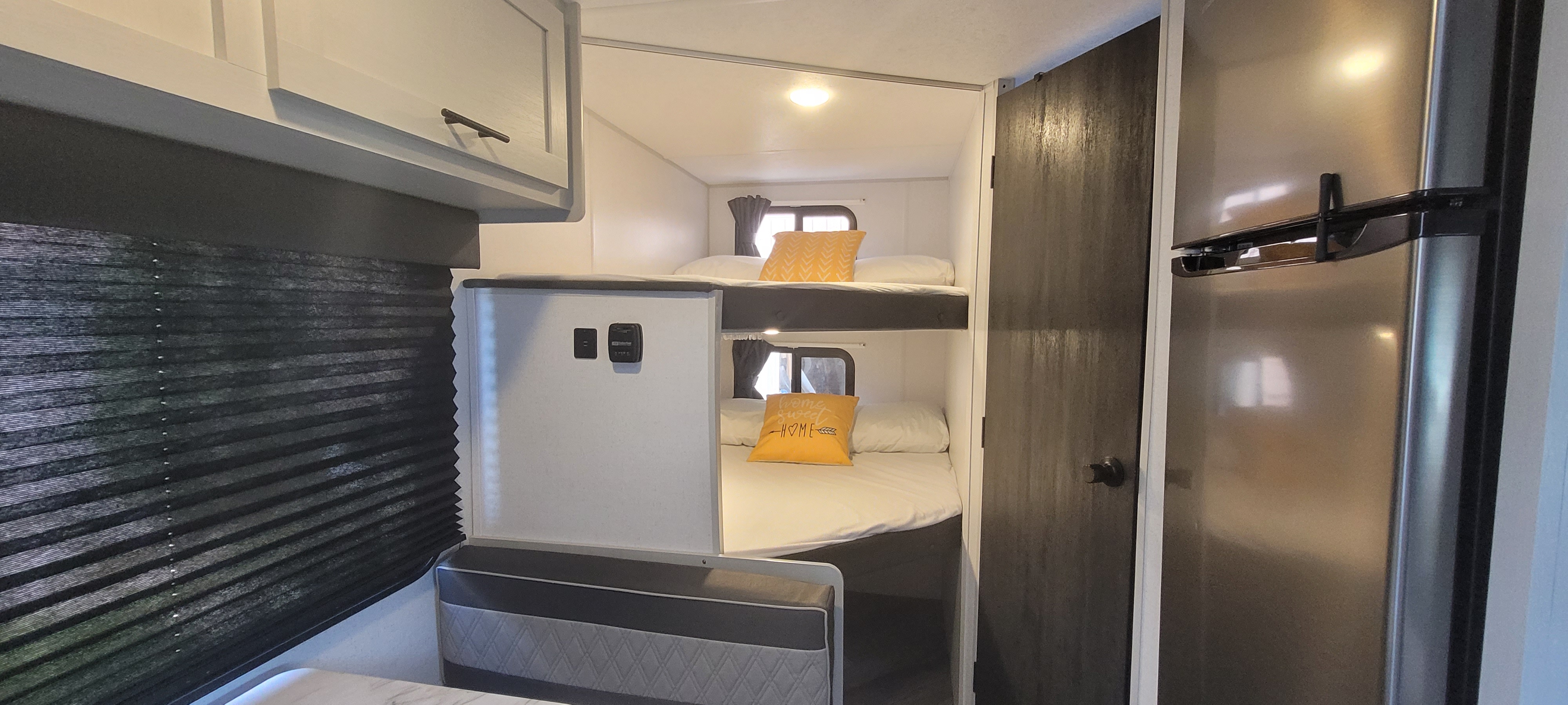 Inside this RV rental, comfortable bunk beds with yellow pillows, a stainless steel fridge, and dark pleated blinds are visible.. Forest River Salem FSX 2022