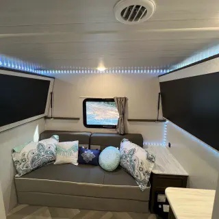 RV rental living area: A grey sofa bed with patterned pillows, illuminated by LED strips. A window offers outdoor views.. Forest River Salem Cruise Lite 2022