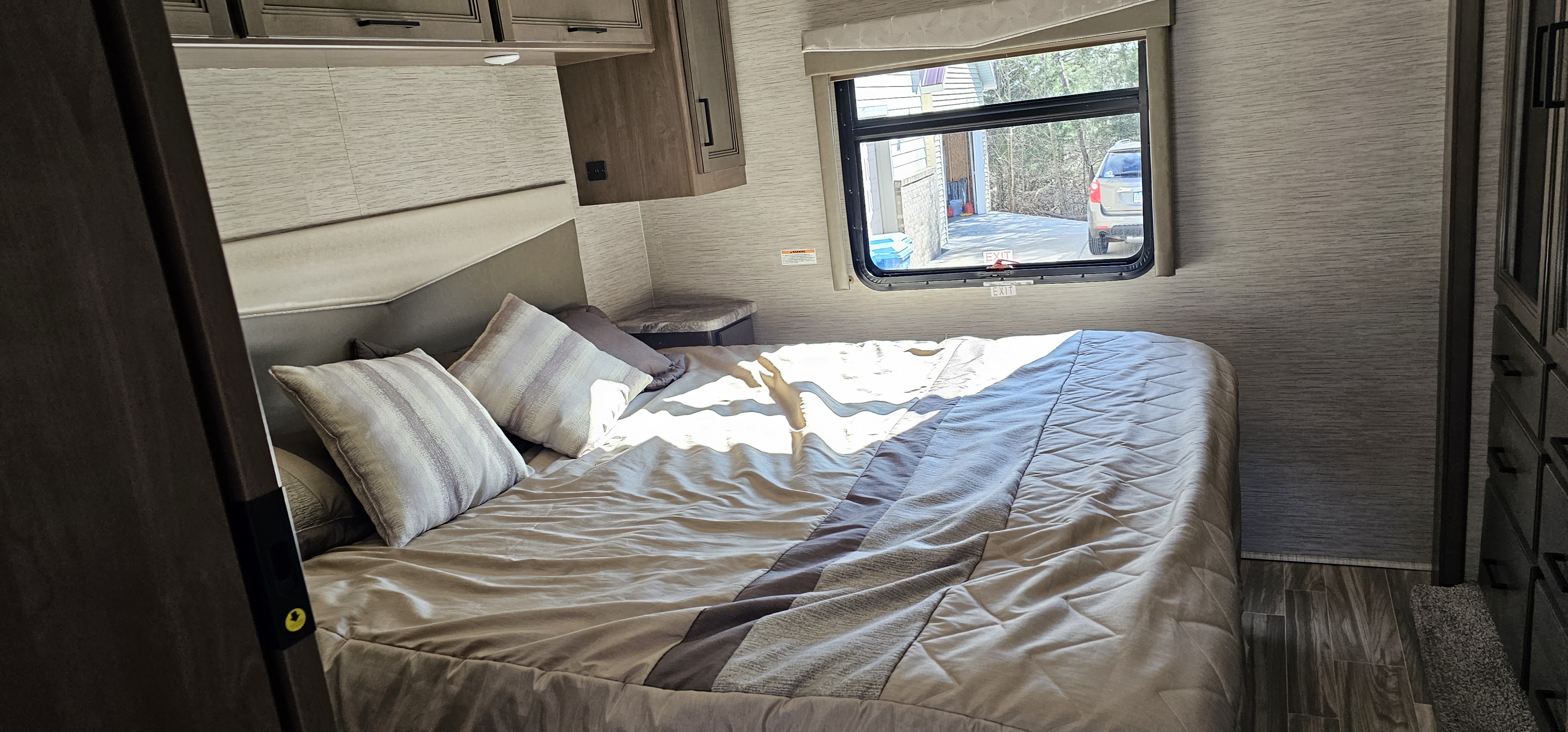 Cozy RV rental bedroom featuring a comfortable bed, overhead cabinets, and a window view, perfect for travel.. Thor A.C.E. 2022