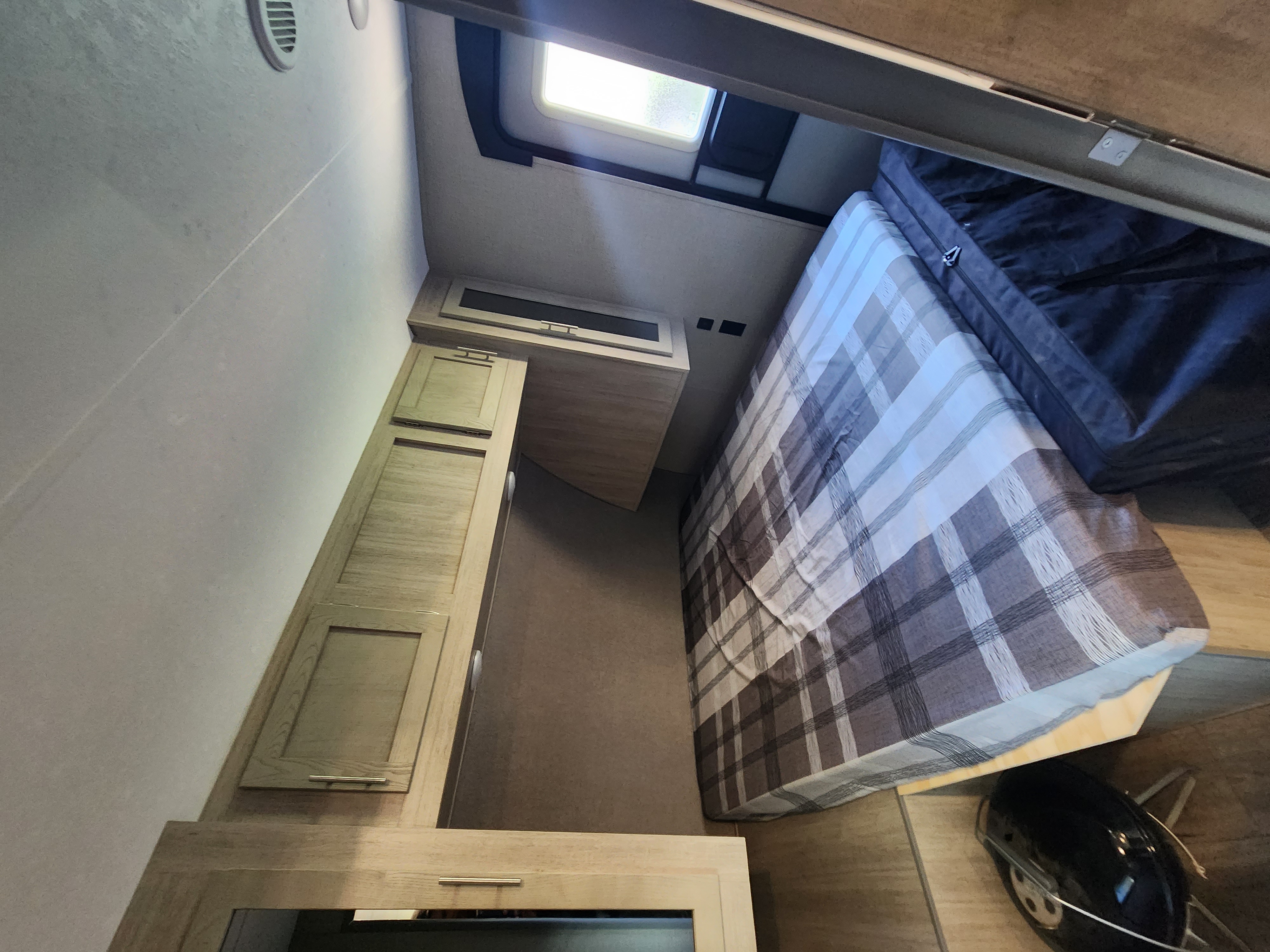 Cozy rv rental bedroom interior, featuring a bed with plaid comforter, wood cabinets, and a bright window.. Coachmen Catalina 263 bunk 2022