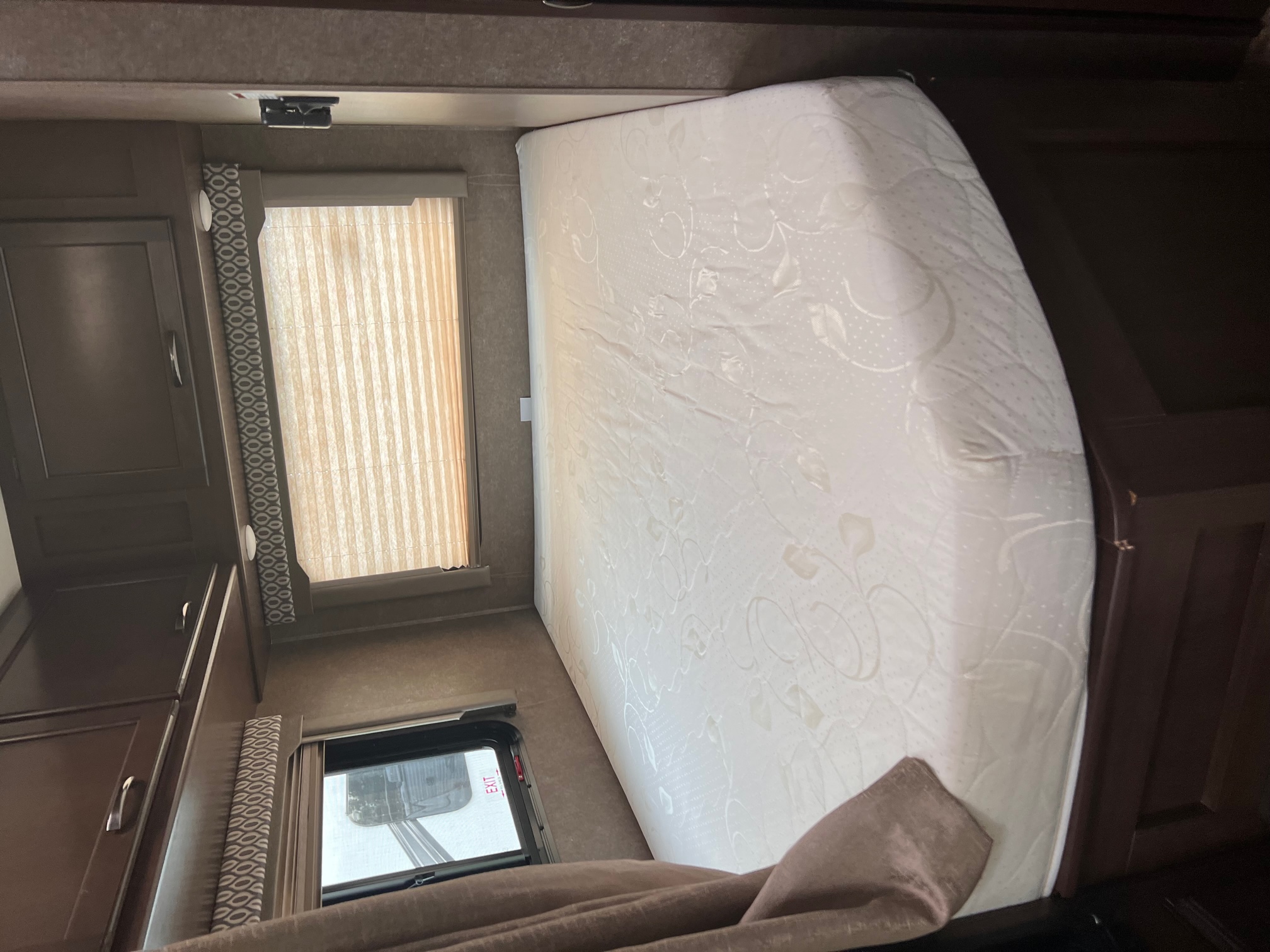 RV rental bedroom showing a white mattress, dark wood cabinets, and windows with blinds.. Thor Freedom Elite 2020