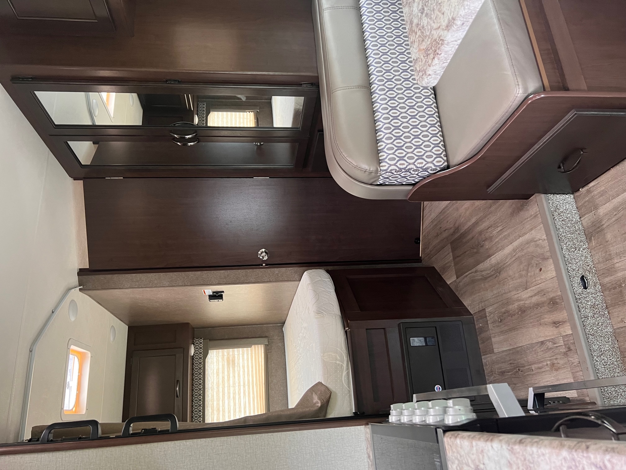 RV rental interior features a patterned dinette, overhead bunk, dark wood cabinetry, and a control panel.. Thor Freedom Elite 2020