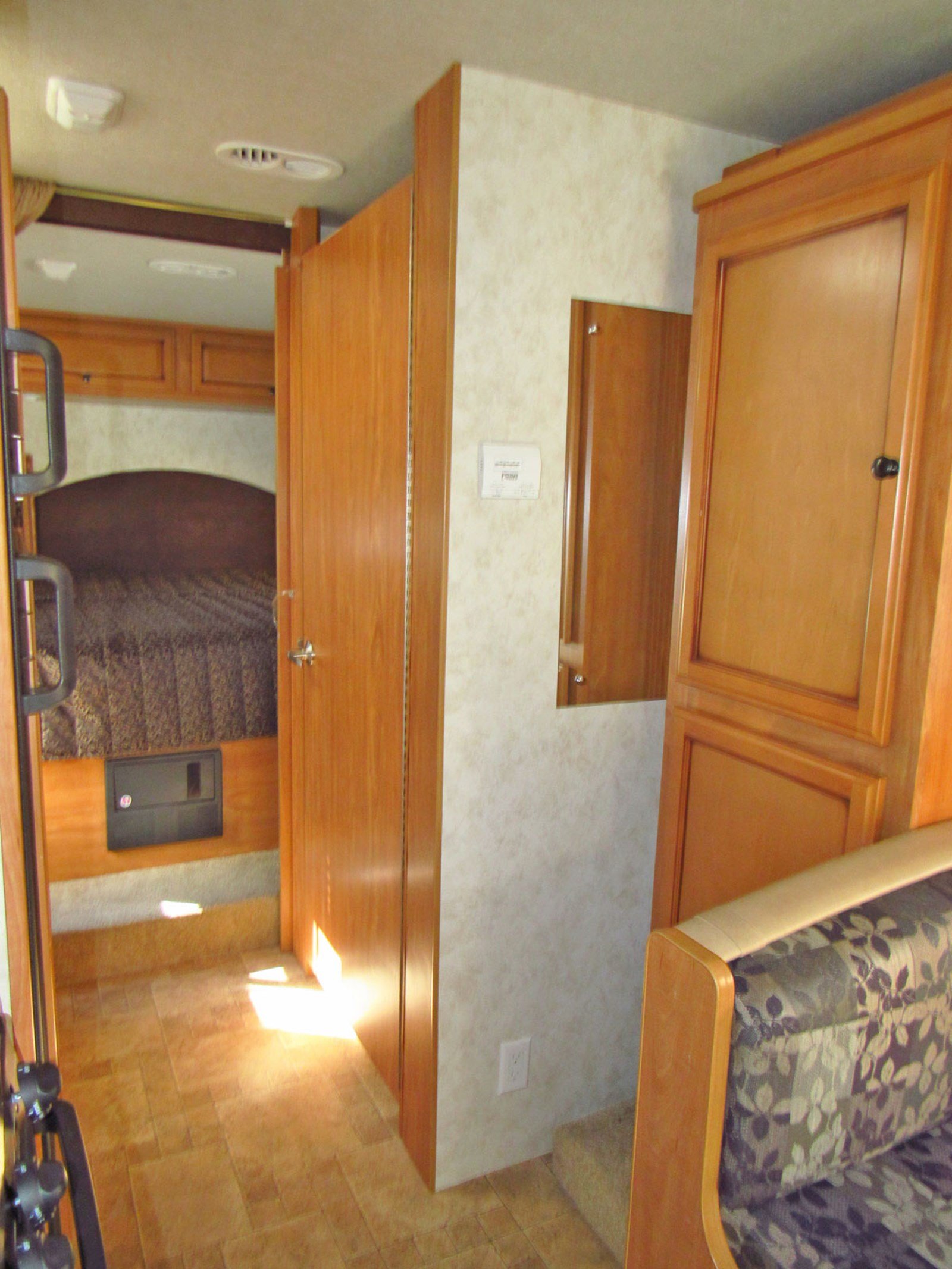 Interior of an RV rental: a compact living and bedroom area with wood-toned cabinets, tiled floor, and patterned sofa.. Tioga Ranger 2011