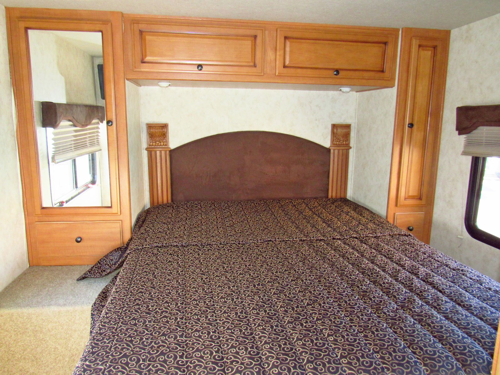 Cozy RV rental bedroom featuring a full-size bed, upholstered headboard, and wood cabinetry with a mirrored wardrobe.. Tioga Ranger 2011