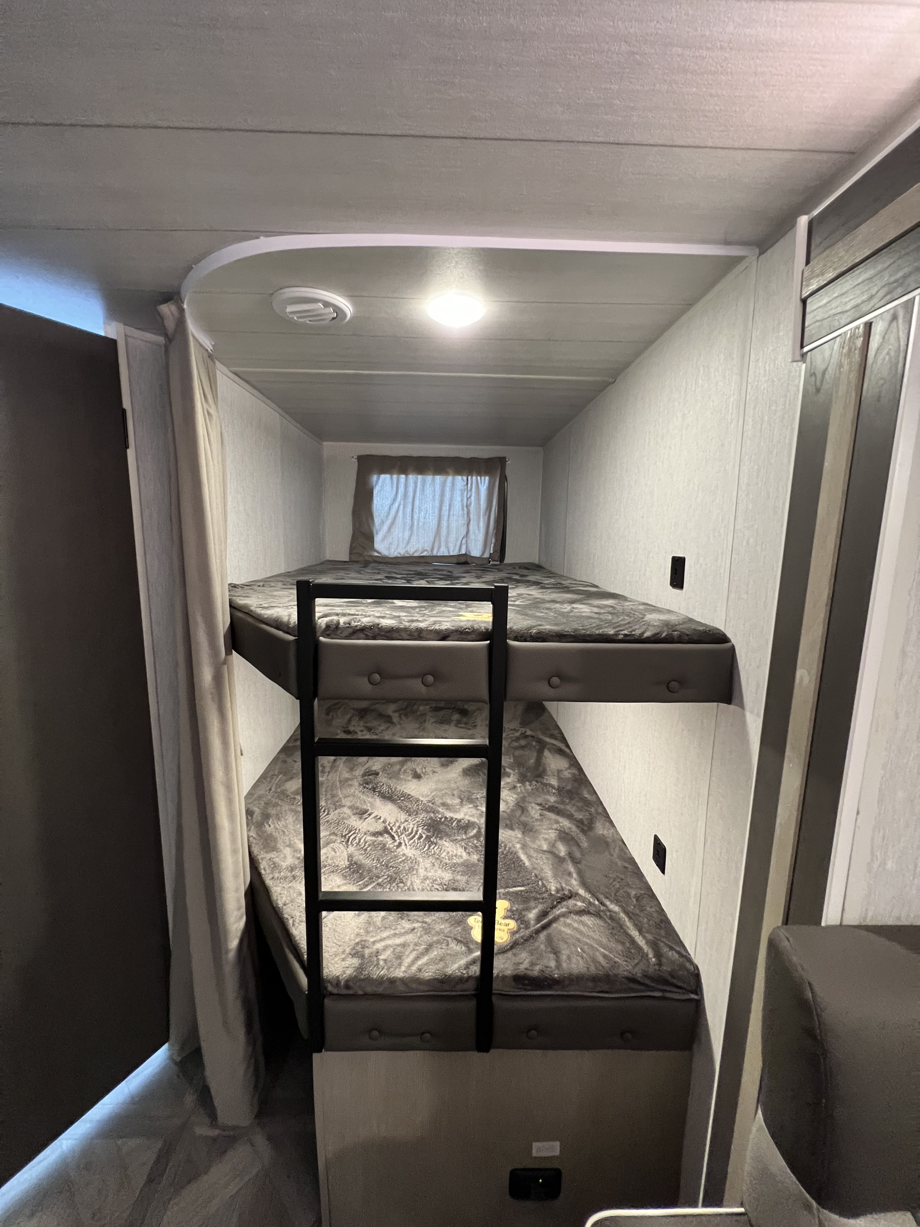 Inside an RV rental: cozy bunk beds with gray blankets, a ladder, and overhead lighting for compact sleeping.. Forest River Salem cruise lite 2023