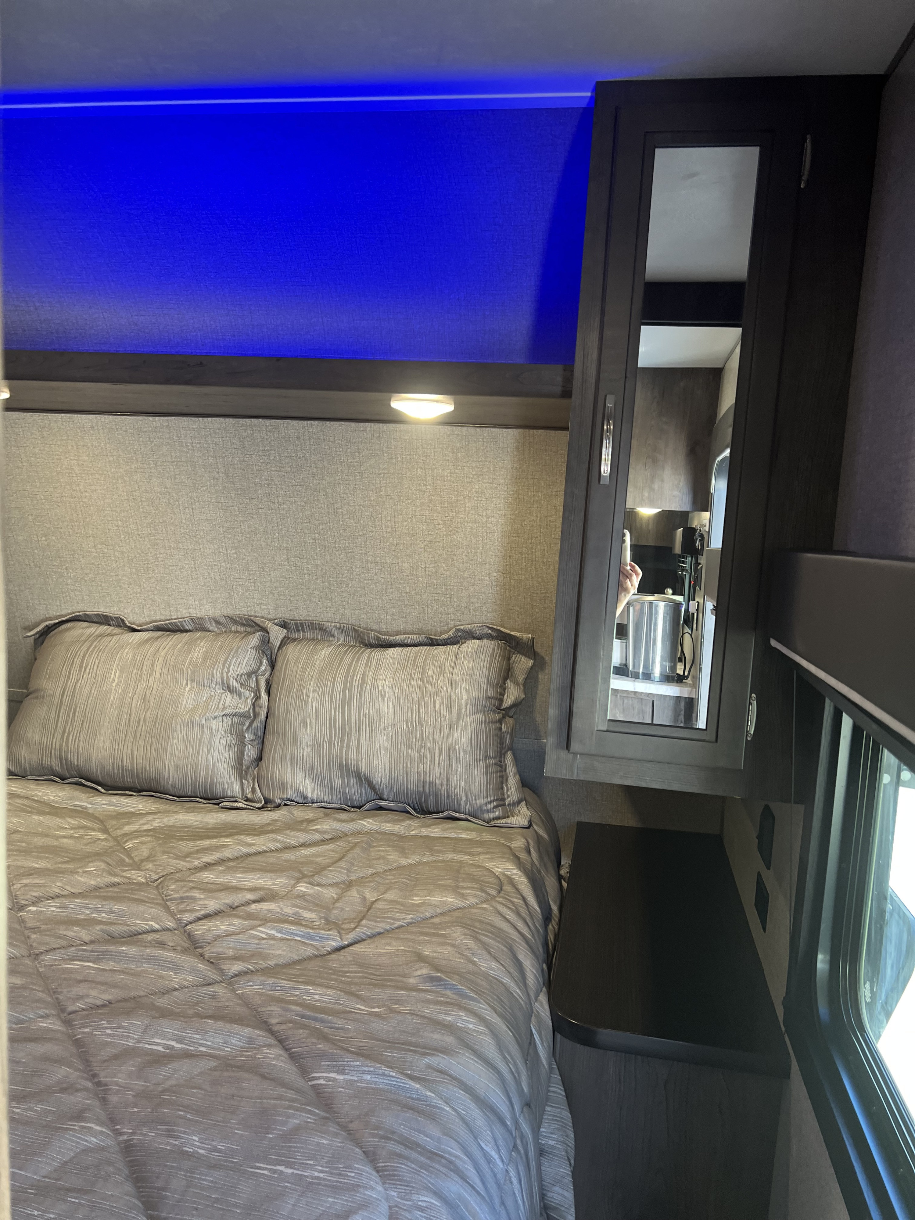 Inside a modern RV rental: a compact bedroom featuring gray bedding, a textured headboard, blue accent lighting, and a mirrored cabinet.. Jayco Jay Flight SLX Rocky Mountain Edition 2021