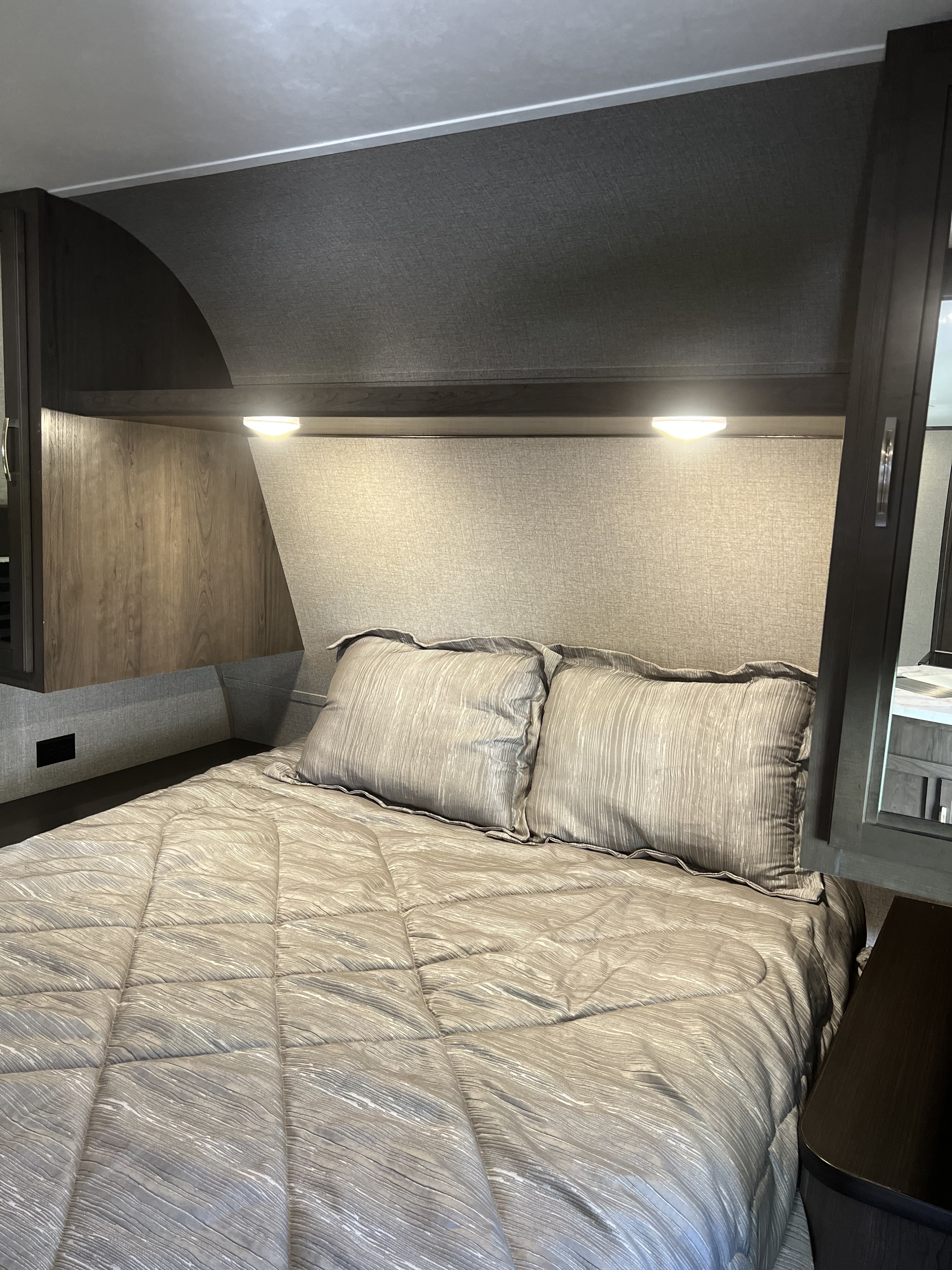 Cozy RV rental bedroom featuring a bed with patterned comforter & pillows, overhead cabinets, and reading lights.. Jayco Jay Flight SLX Rocky Mountain Edition 2021