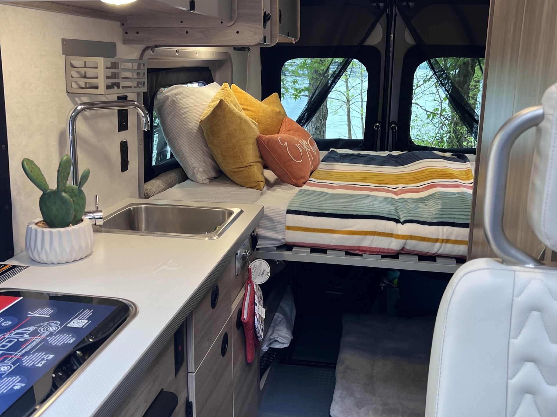 Cozy rv rental interior featuring a well-appointed kitchenette, bed with colorful pillows, and serene lake views from the back.. Winnebago SOLIS 59 PX 2023
