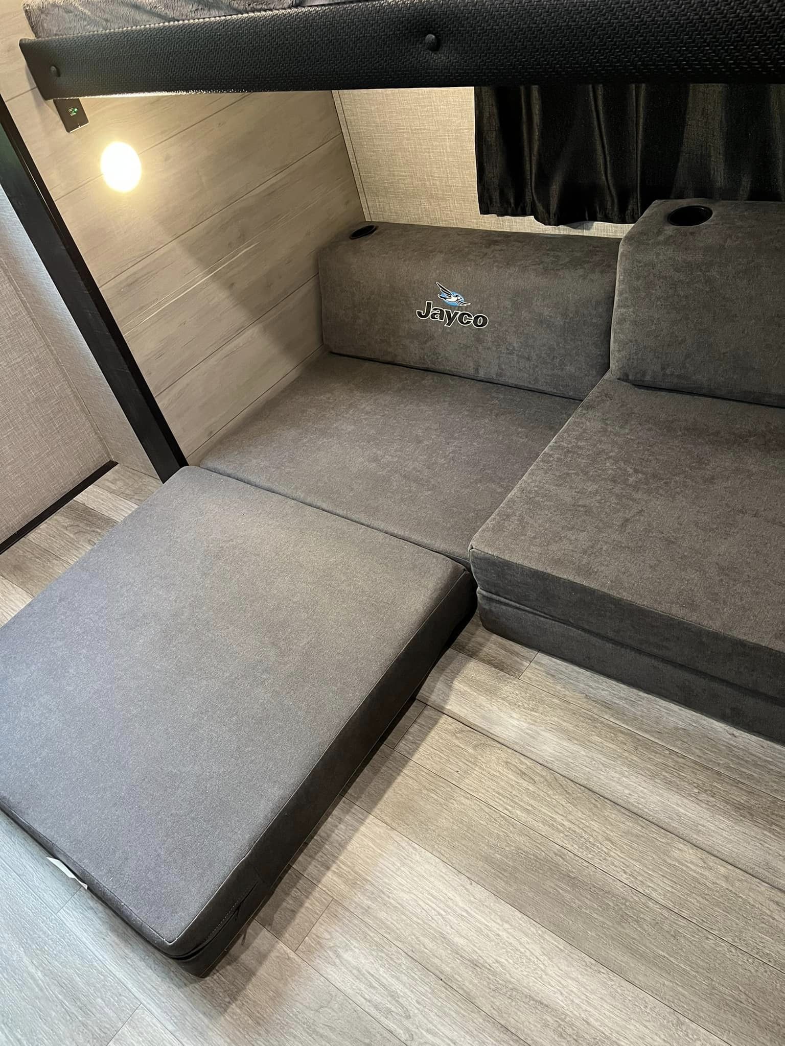 Inside an RV rental: versatile gray modular seating with Jayco logo, converting to a bed. Light wood-look interior, with bunk above.. Jayco Jay Flight SLX 2022