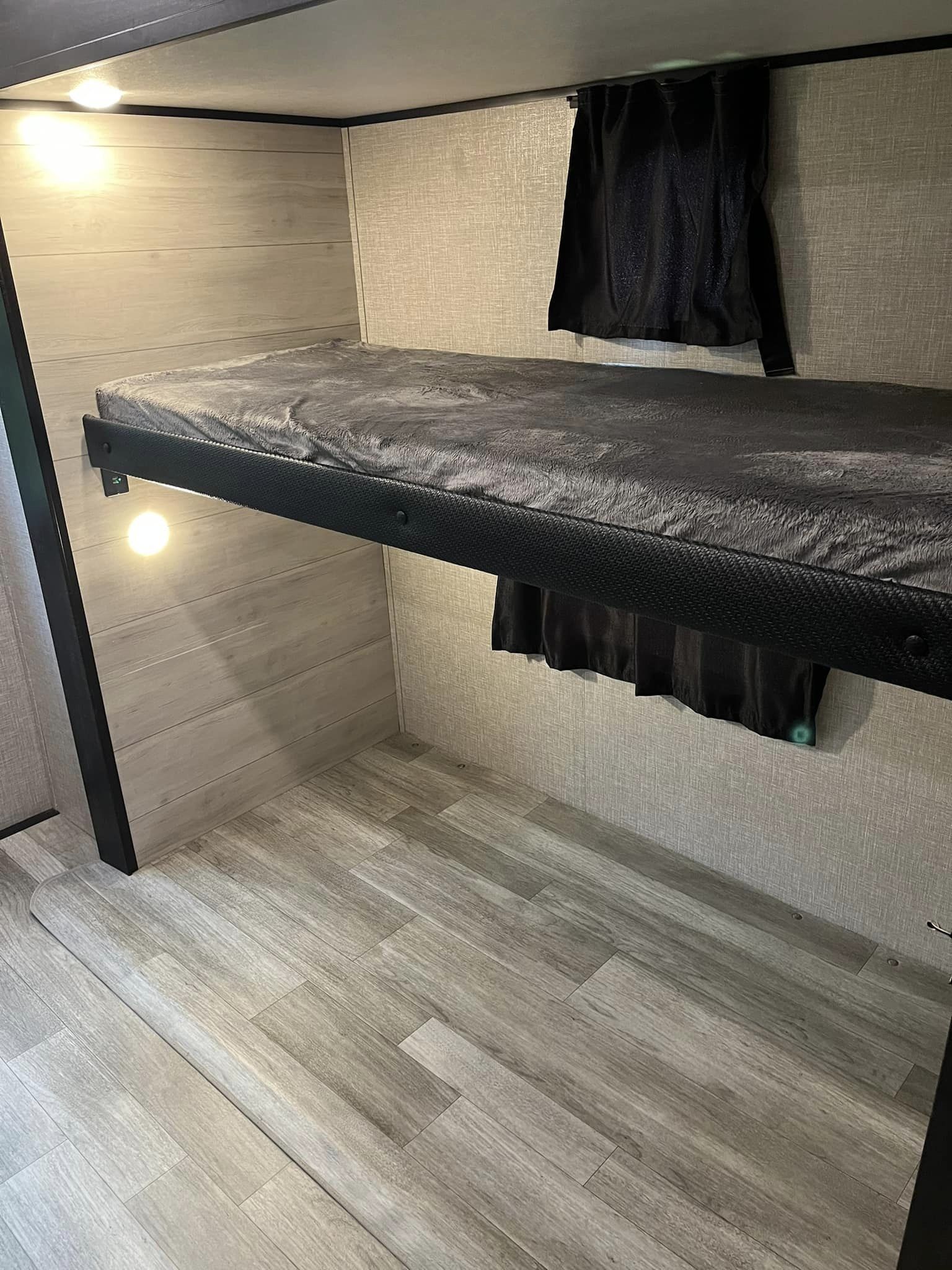Inside an RV rental: a lower bunk bed with dark bedding, under-bunk lighting, wood-style walls, and privacy curtain.. Jayco Jay Flight SLX 2022