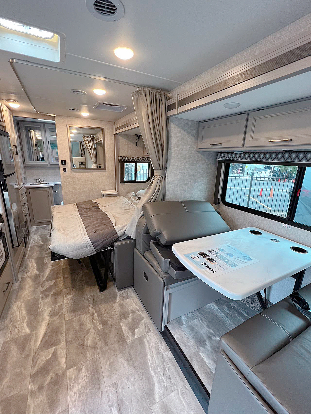 Modern RV rental interior featuring a cozy fold-out bed, dinette table, and compact kitchen area for comfortable travel.. Thor Quantum 2023