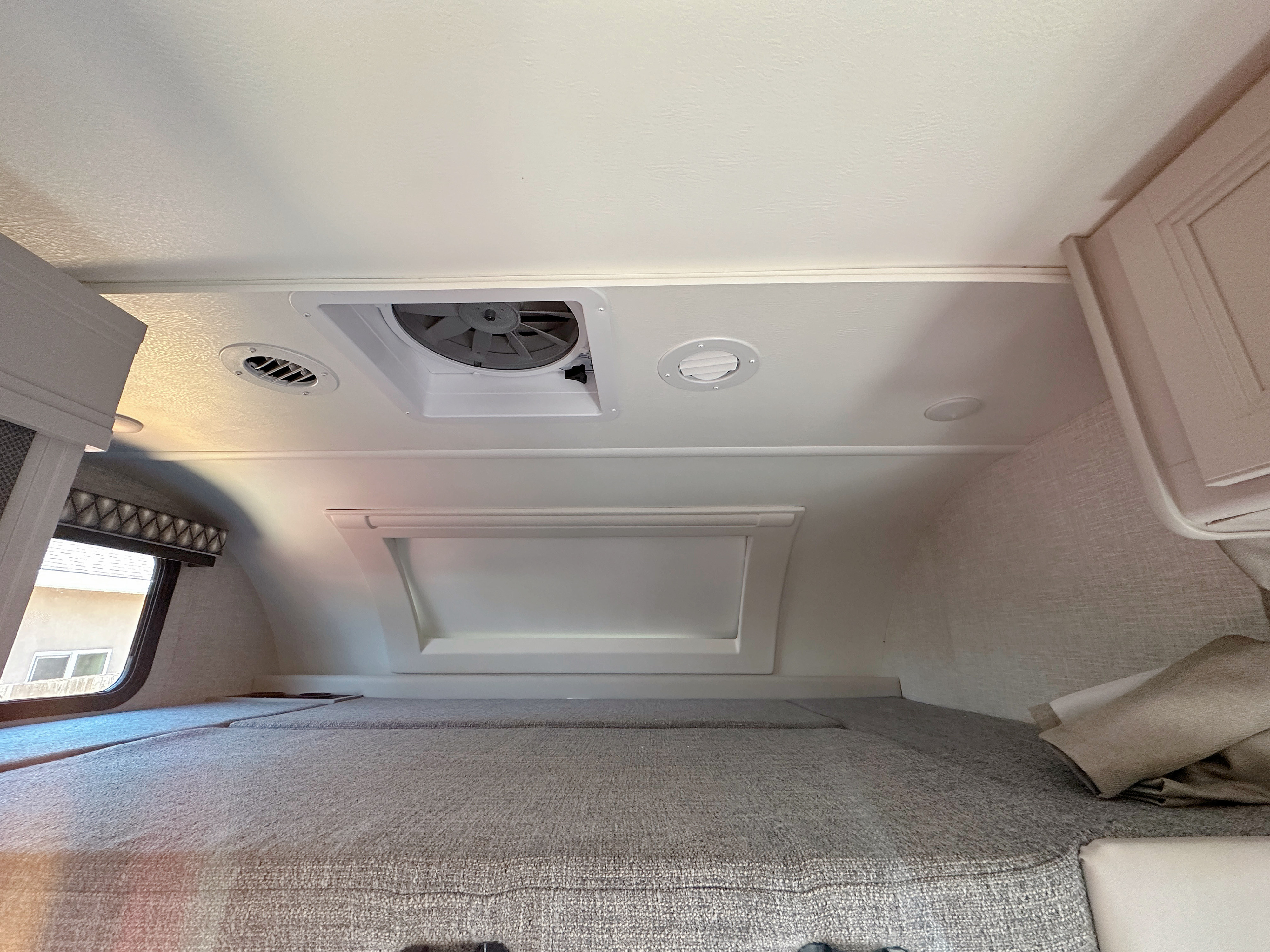 Overhead sleeping area in an RV rental, showing the mattress, window, ceiling fan, and air vents.. Thor Quantum 2023
