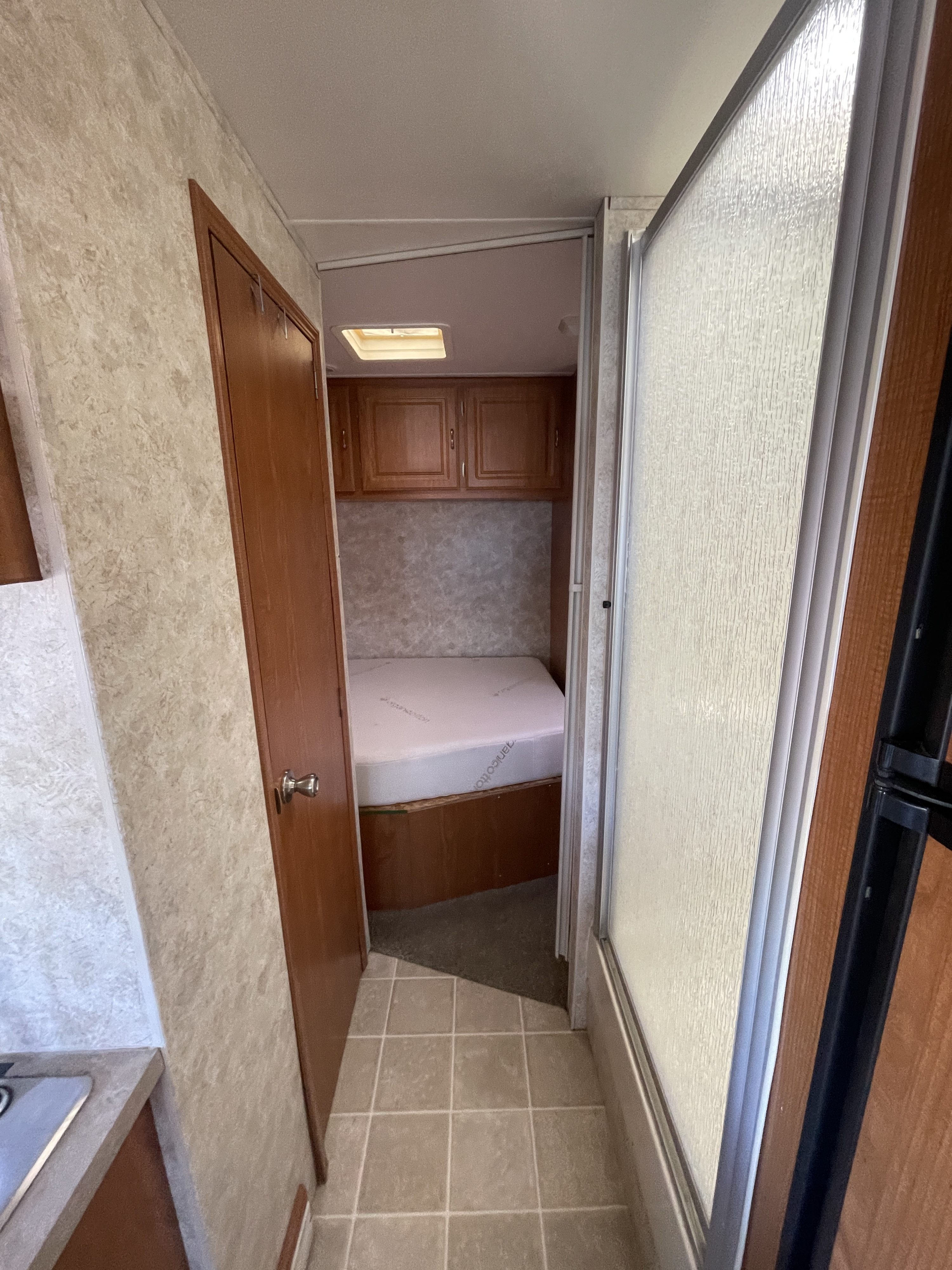 RV rental interior: Hallway view to a bedroom with bed, cabinets, and skylight. Shower and a partial kitchenette are also visible.. Coachmen Freelander 2004