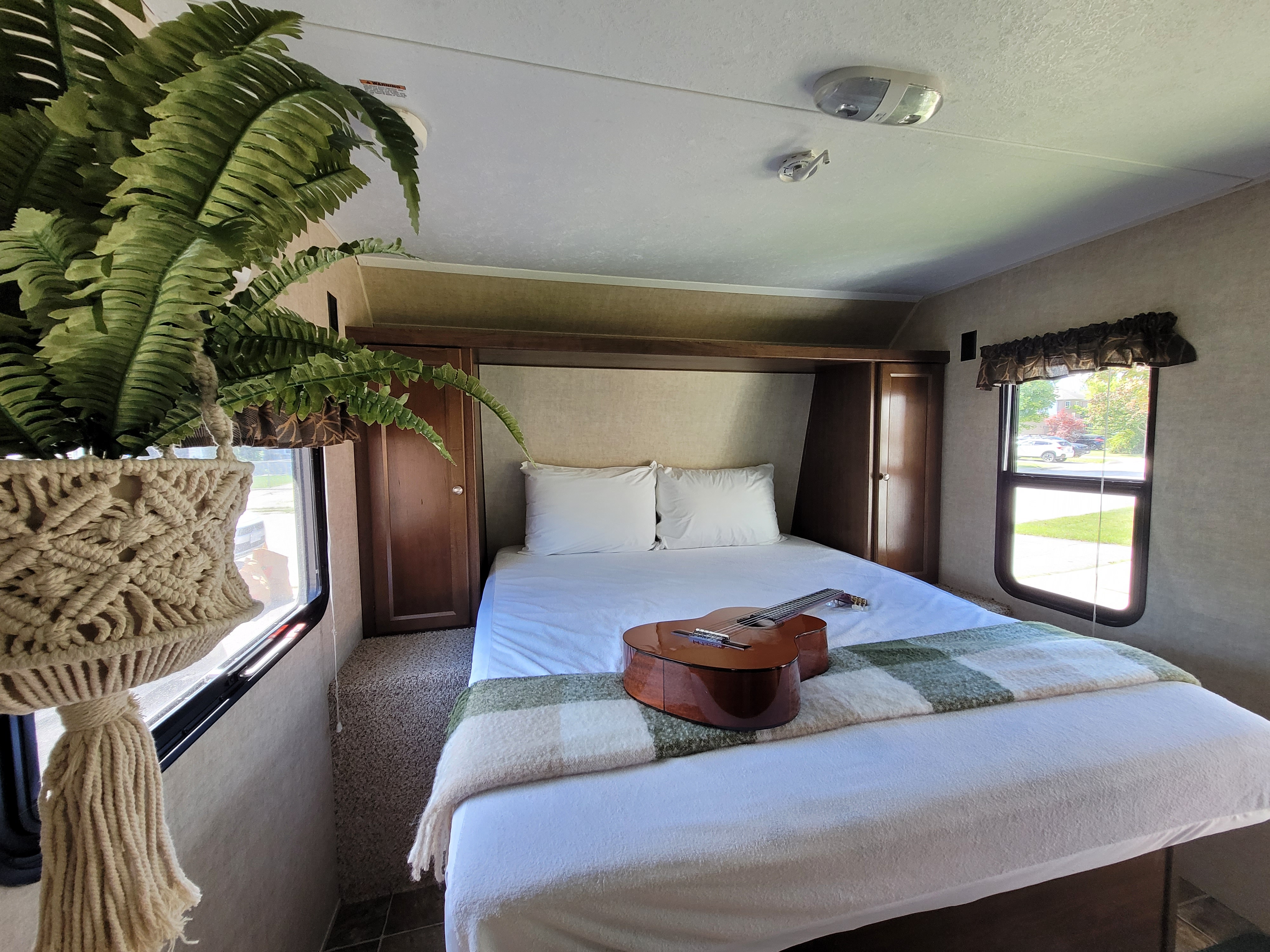 Serene RV rental bedroom: comfy bed, classical guitar, and a hanging fern plant by the window.. Keystone RV Hideout LHS 2016