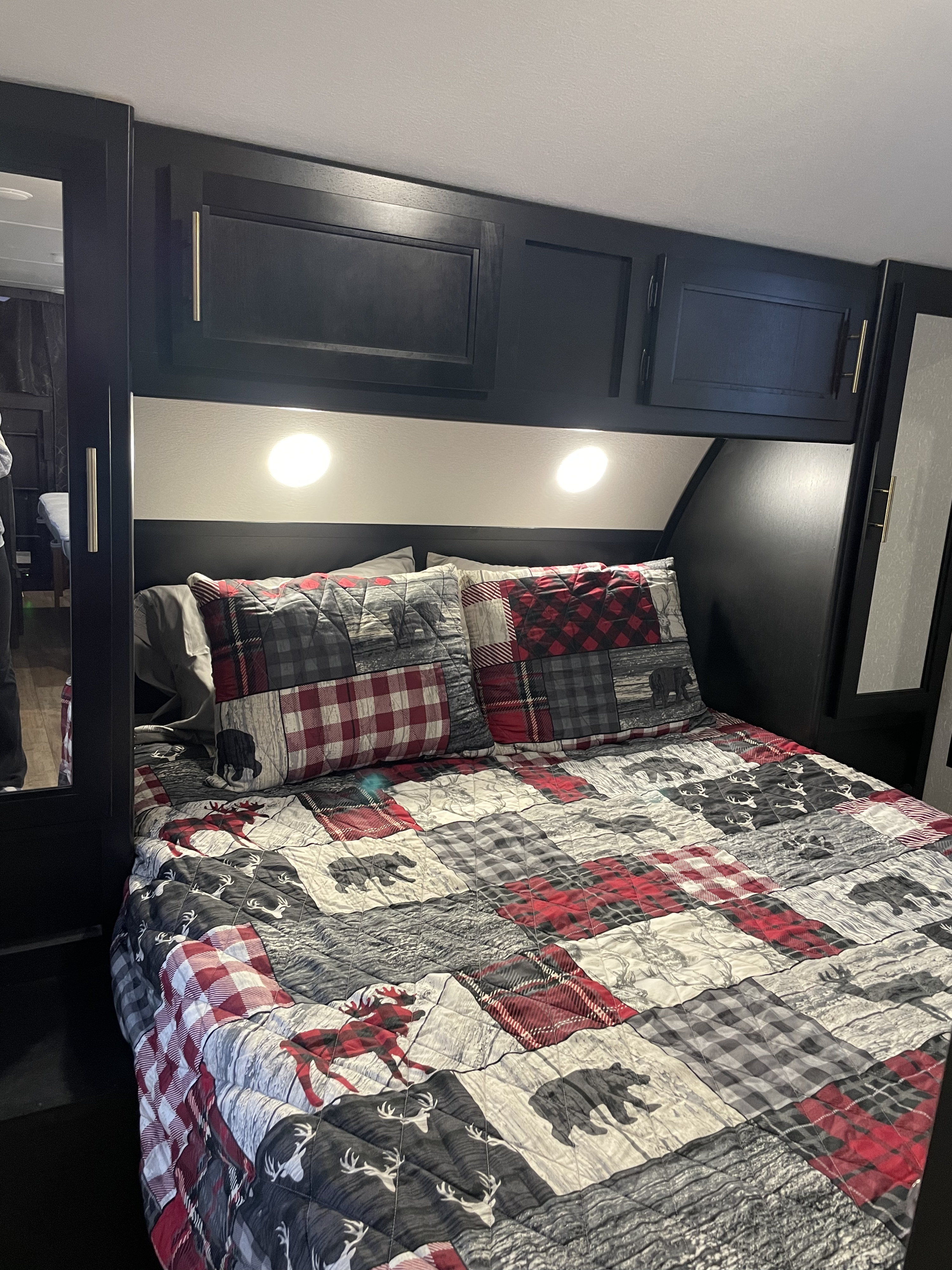 Cozy RV rental bedroom with plaid and bear-patterned bedding, overhead cabinets, and reading lights, ready for adventure.. Forest River Cherokee Grey Wolf 2022