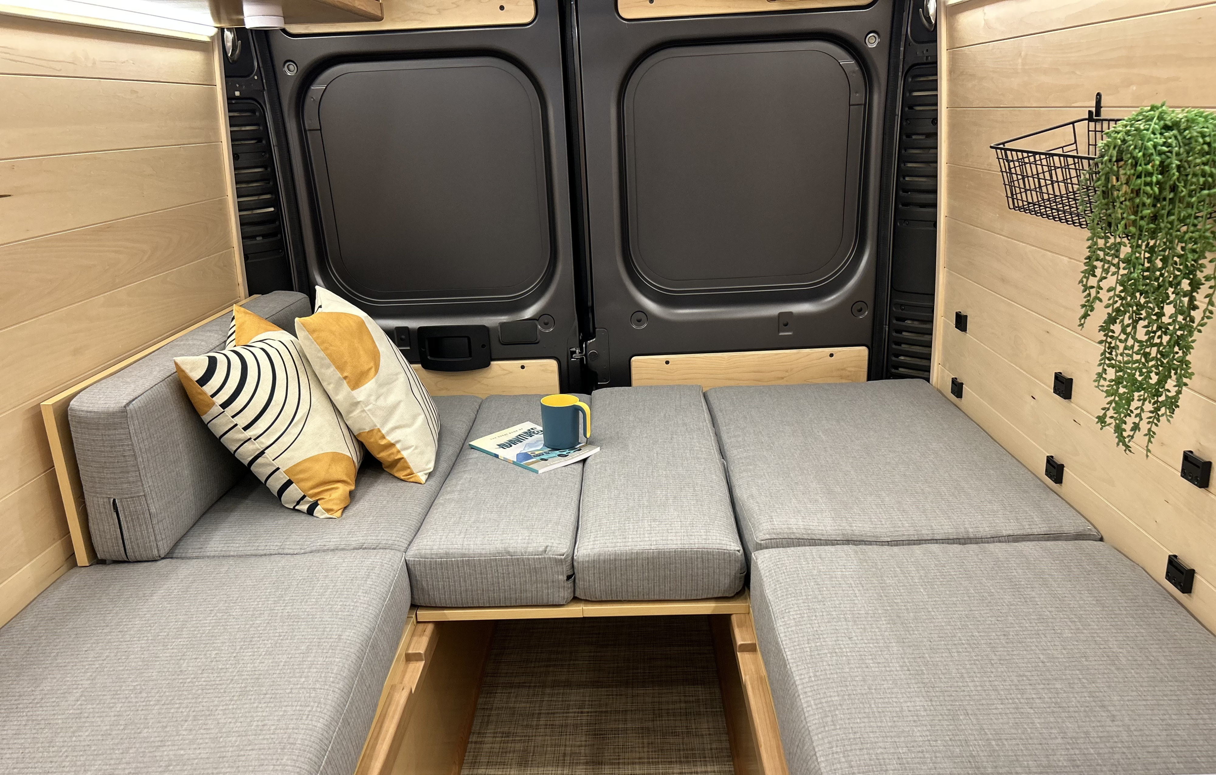 RV rental camper van interior featuring modular gray cushions that convert to a bed, light wood walls, and rear doors.. Dodge Ram Promaster 3500 Promaster 2022
