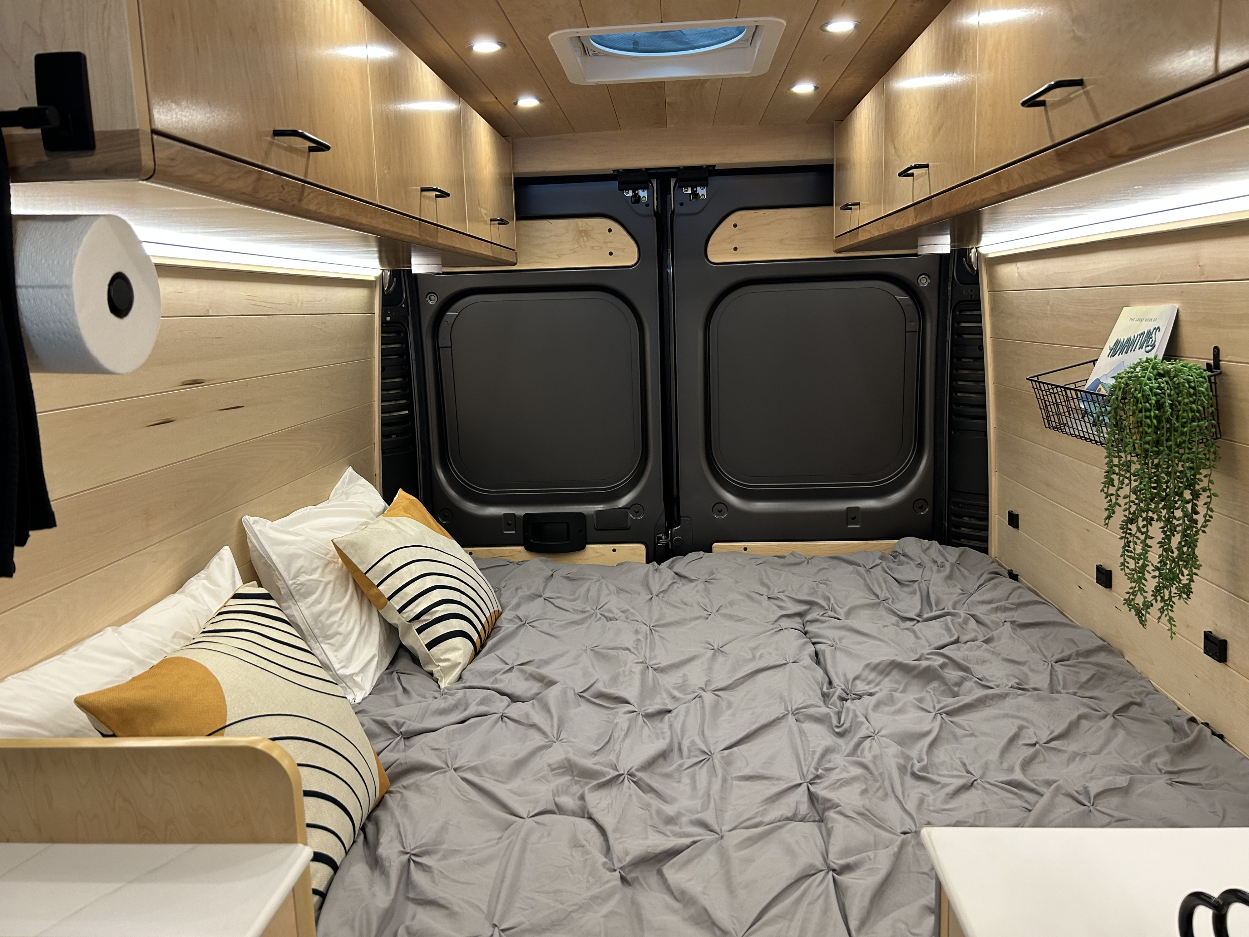 Cozy RV rental bedroom with wood paneling, overhead cabinets, and a comfy bed. Perfect for van life adventures!. Dodge Ram Promaster 3500 Promaster 2022