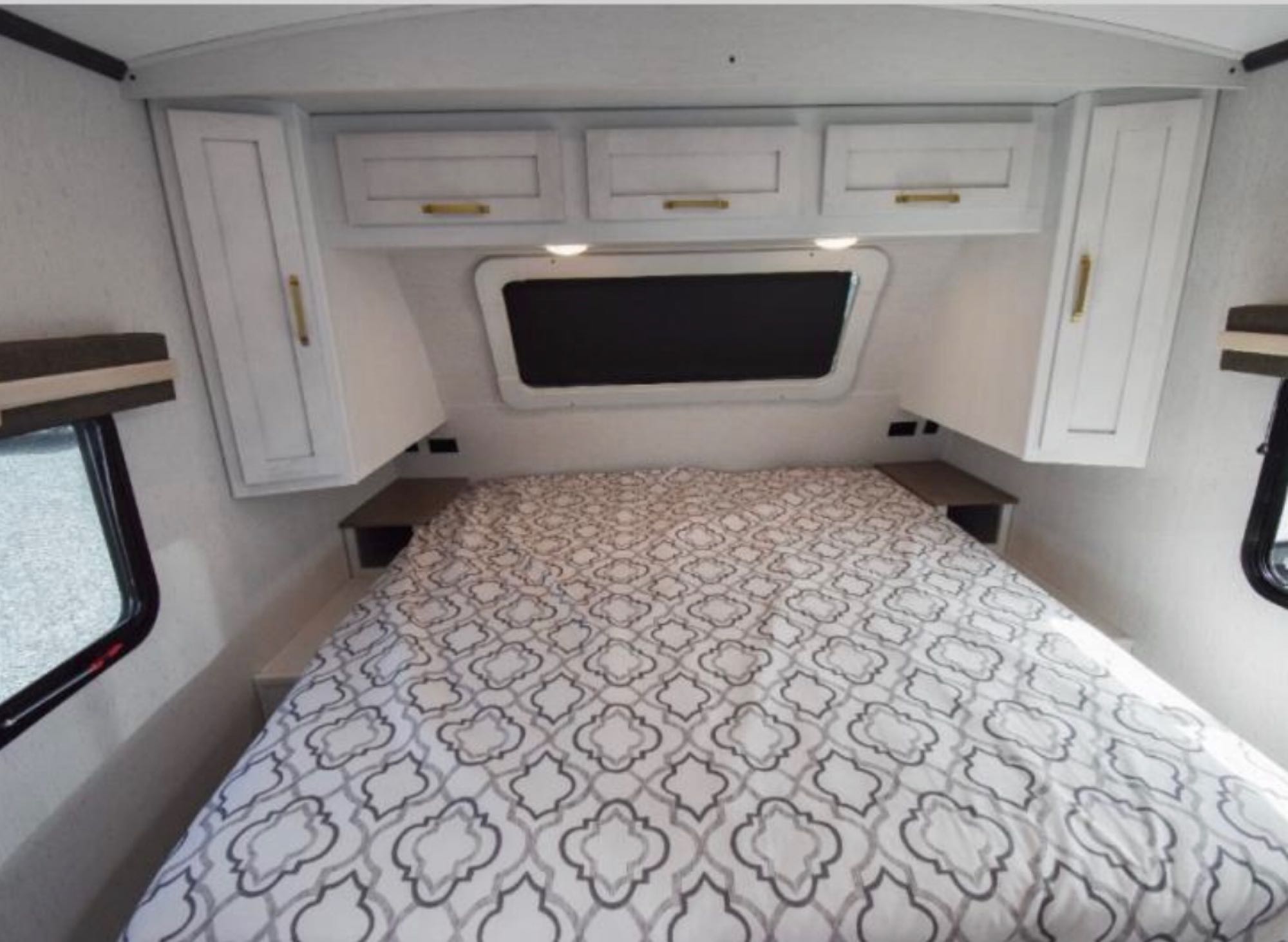 Spacious RV rental bedroom with white overhead cabinets, a comfortable patterned bed, and side windows.. Astoria Astoria Trailer 2022