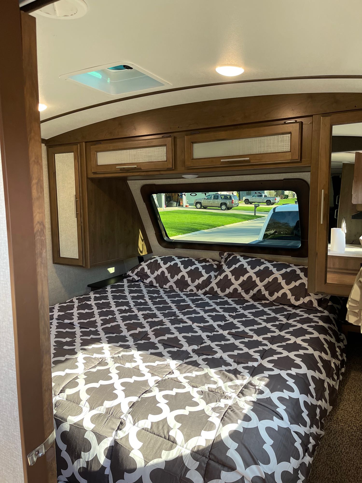 Inviting RV rental bedroom with patterned bed, wood cabinets, and a window offering a bright street view.. Keystone Cougar Half-Ton 2019
