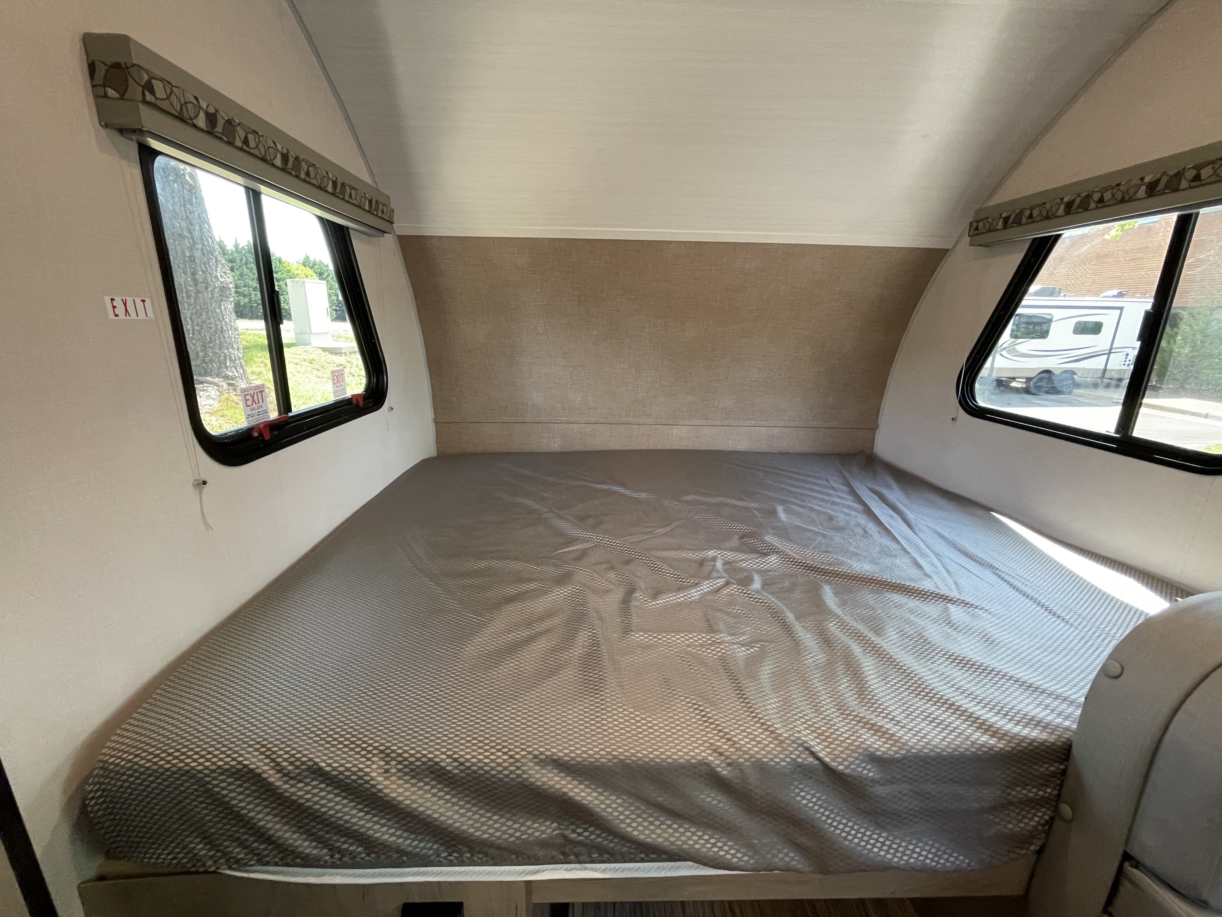 RV rental bed area with a comfortable mattress, soft headboard, and dual windows offering outdoor views. Find comfort on the road.. Forest River R-Pod 2021