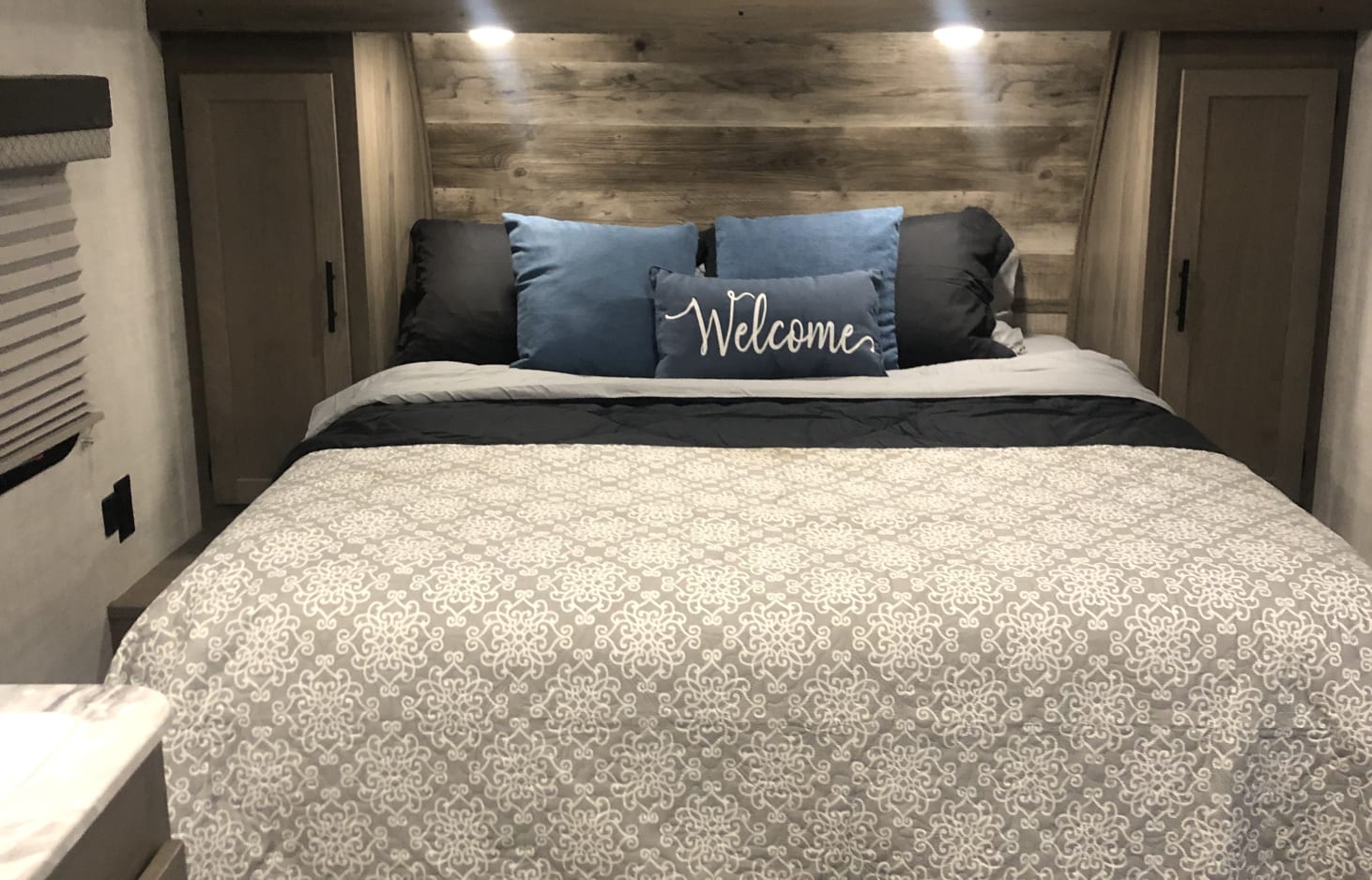 RV rental bedroom featuring a cozy bed, "Welcome" pillow, patterned comforter, and built-in storage.. Gulf Stream Ameri-Lite 2022