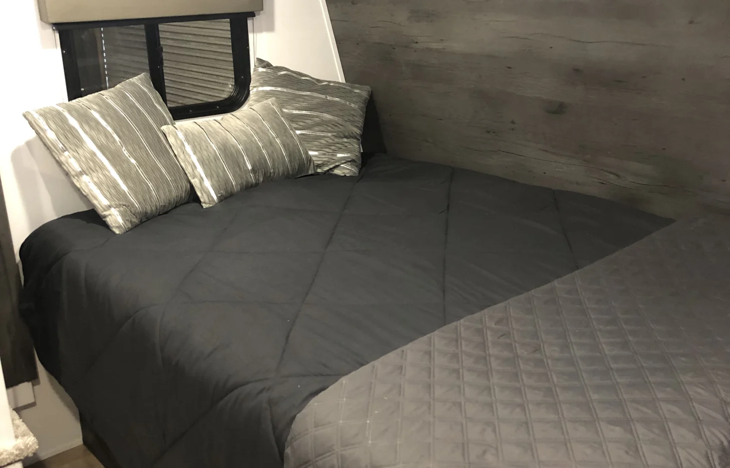 View inside an RV rental showing a neatly made bed with a dark grey comforter and decorative striped pillows.. Keystone RV Hideout 2022