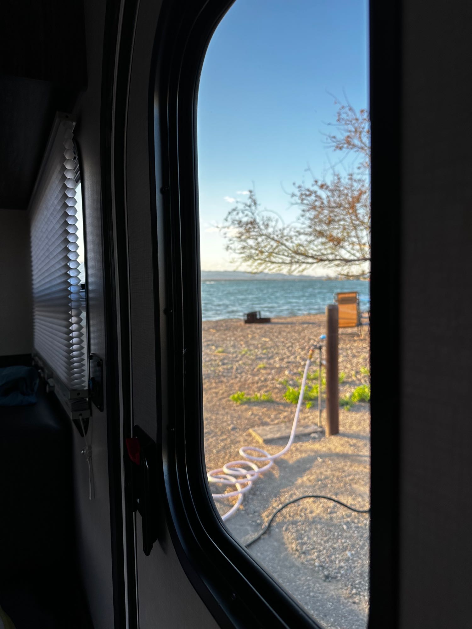 Enjoy this tranquil RV rental view from inside: a window frames a sunny beach leading to a calm lake, surrounded by trees.. InTech RV InTech RV Trailer 2021