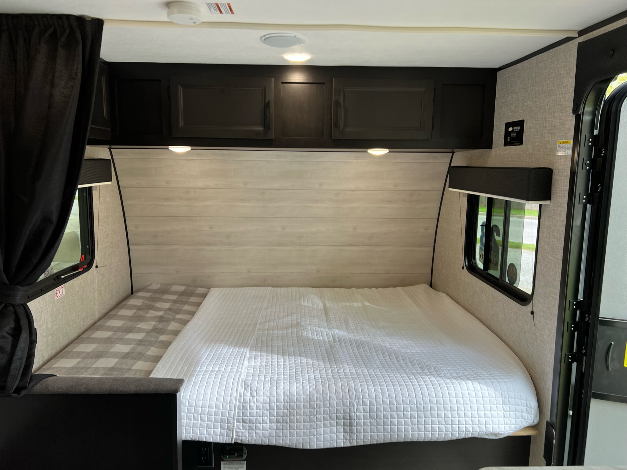 Cozy RV rental bedroom featuring a spacious bed with white bedding, dark cabinets, and windows for a comfortable stay.. Jayco Jay Flight SLX Baja Edition 2022