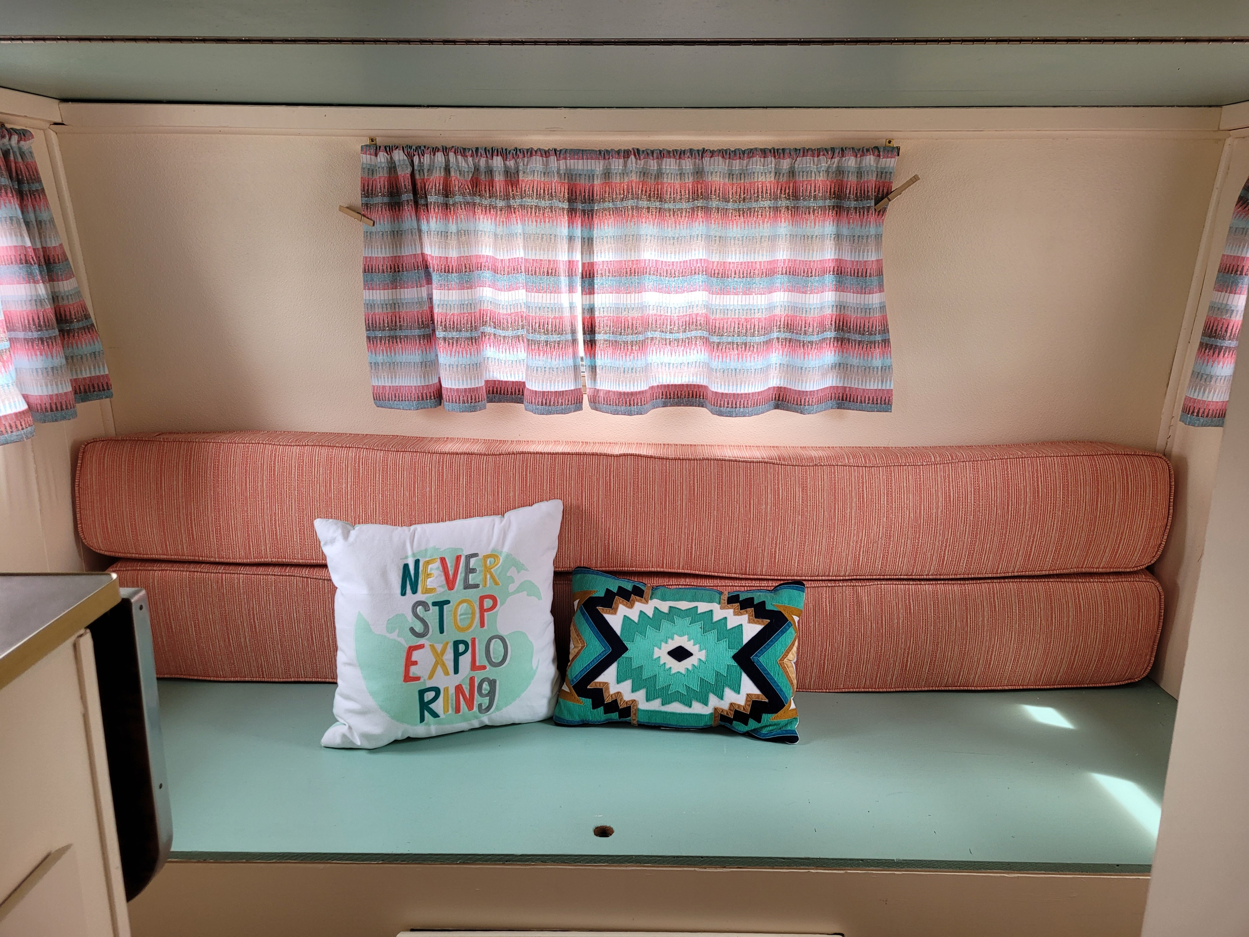 Inside a charming RV rental: striped curtains, coral cushions, and "NEVER STOP EXPLORING" pillow. Perfect for travel.. Concord Vintage 1973