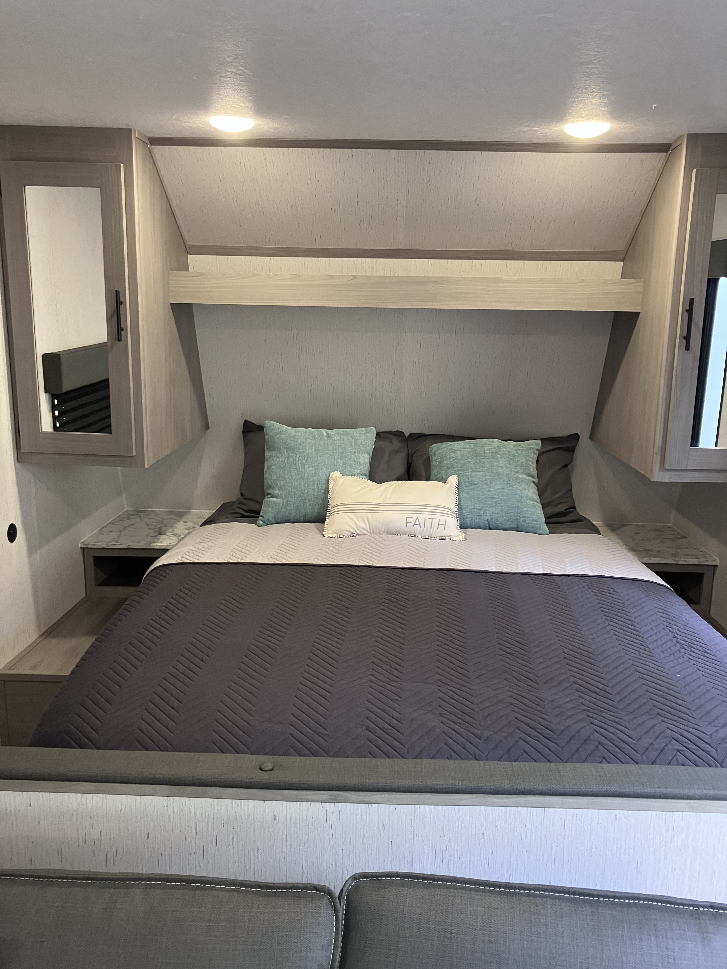 **RV rental** bedroom with a gray comforter, teal pillows, and a 'Faith' pillow.. Dutchmen Coleman Lantern LT 2023