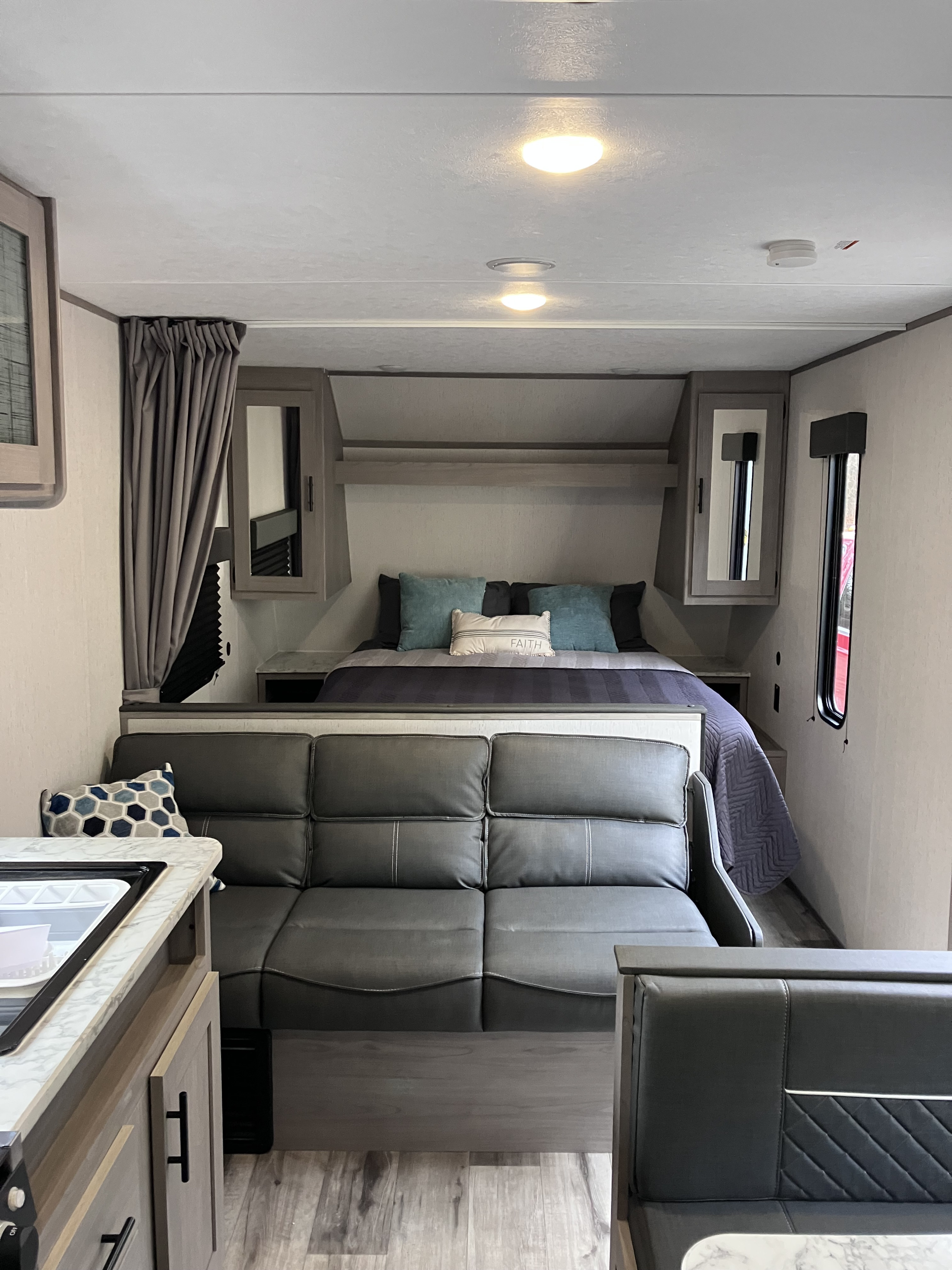 Spacious RV rental interior featuring a cozy bedroom with bed and modern living area with couch and kitchen counter.. Dutchmen Coleman Lantern LT 2023