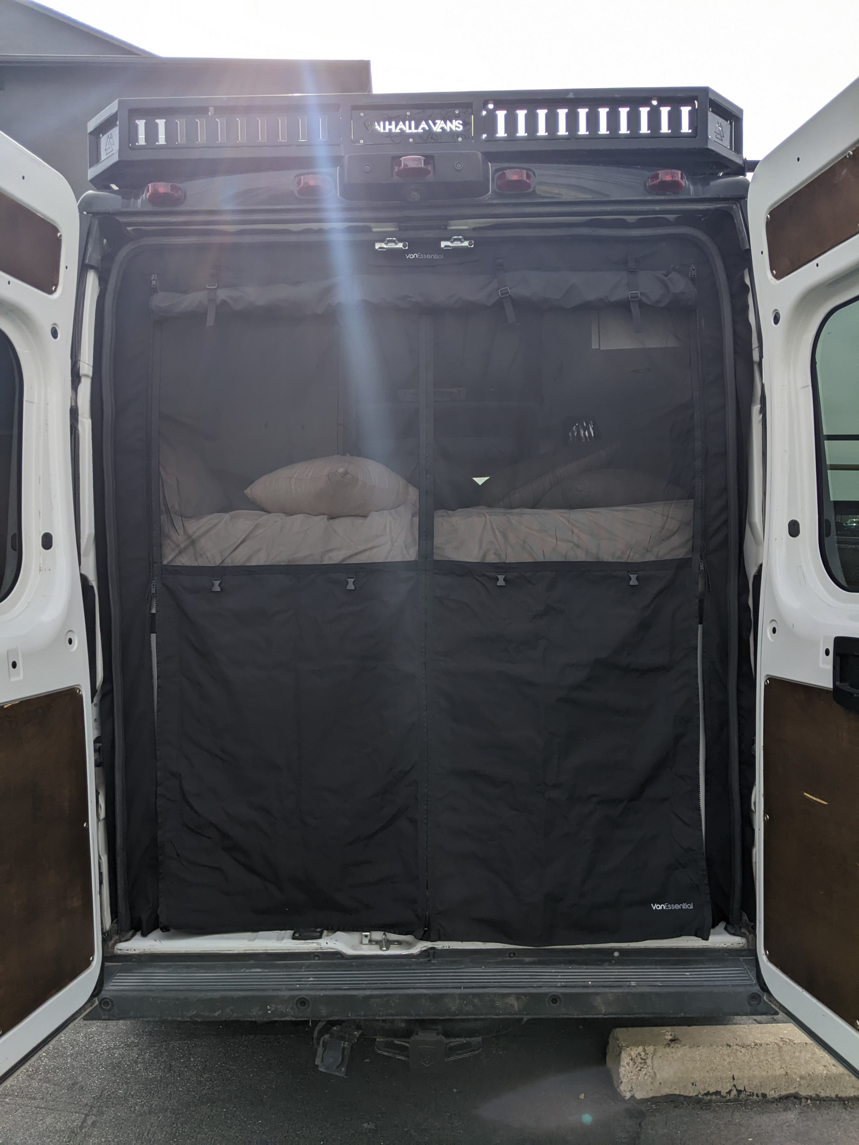 Rear view of an RV rental camper van with open doors, showing a bug screen, dual beds, and a roof rack. Valhalla Vans.. Dodge Sprinter Van 2016