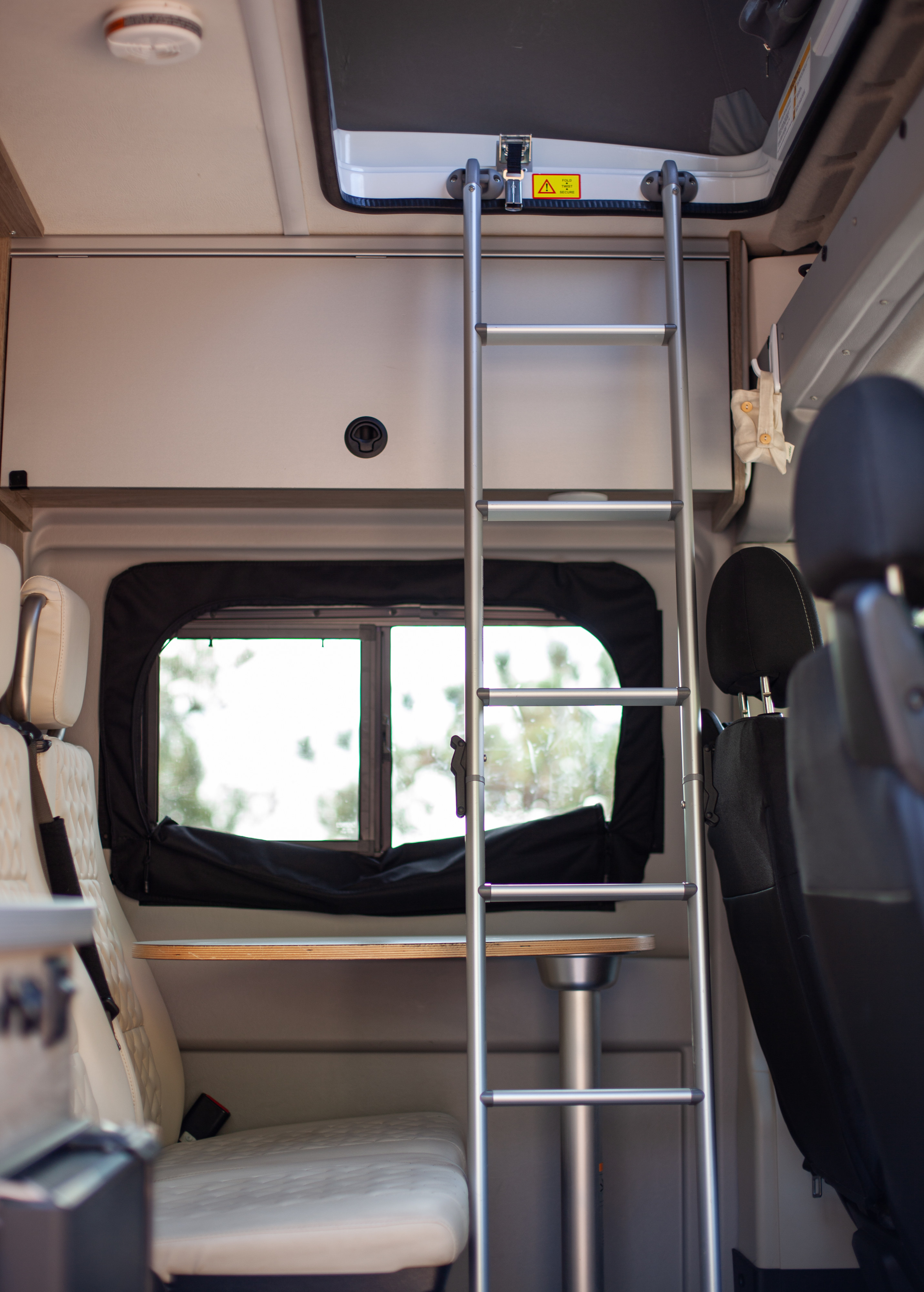 Interior of an RV rental: a ladder to an upper bunk, a table with a sink, and seating, ready for adventure.. Winnebago Solis 2021