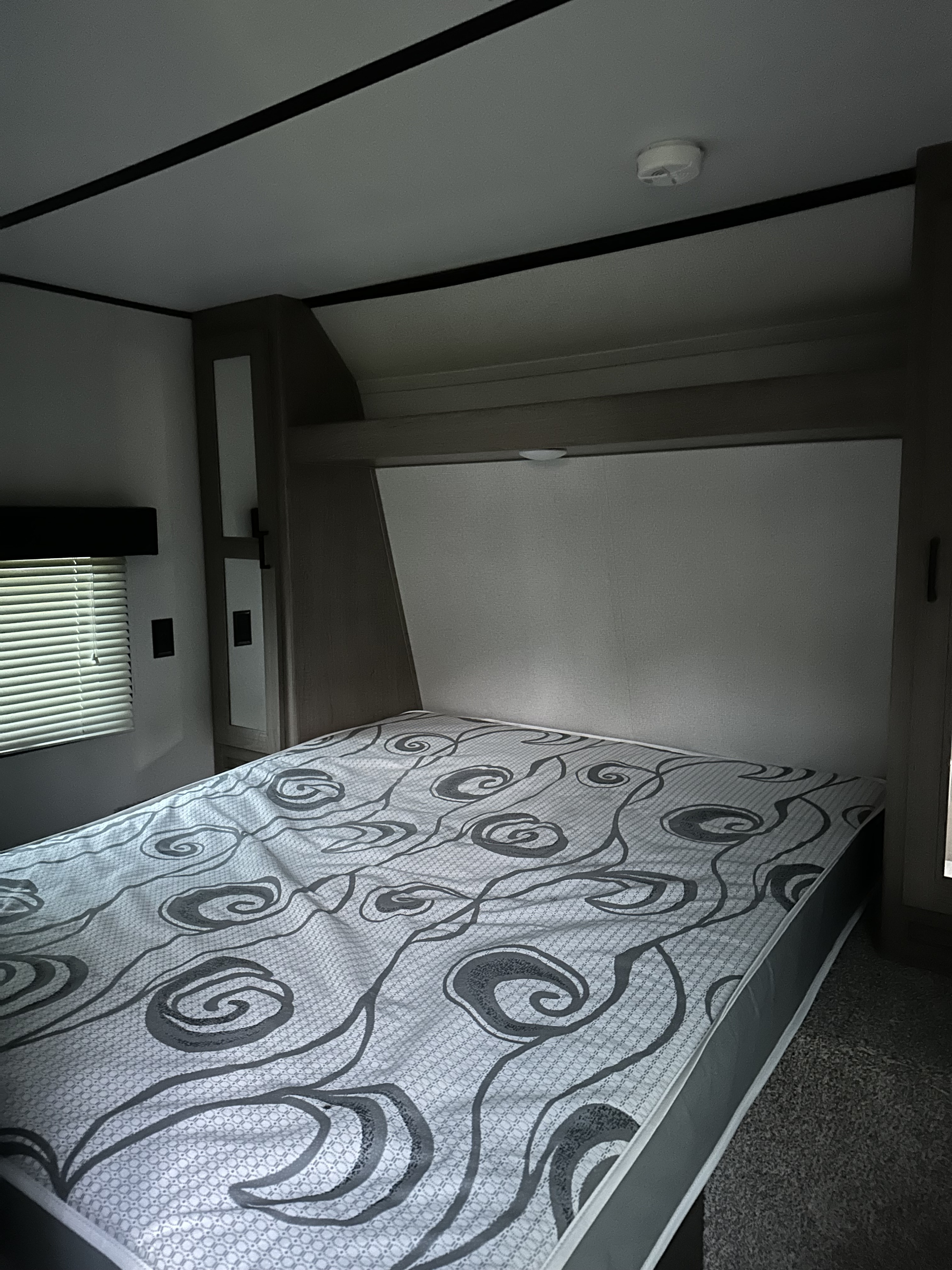 RV rental bedroom with patterned mattress, built-in storage, window blinds, and overhead lighting.. Keystone RV Hideout LHS 2020