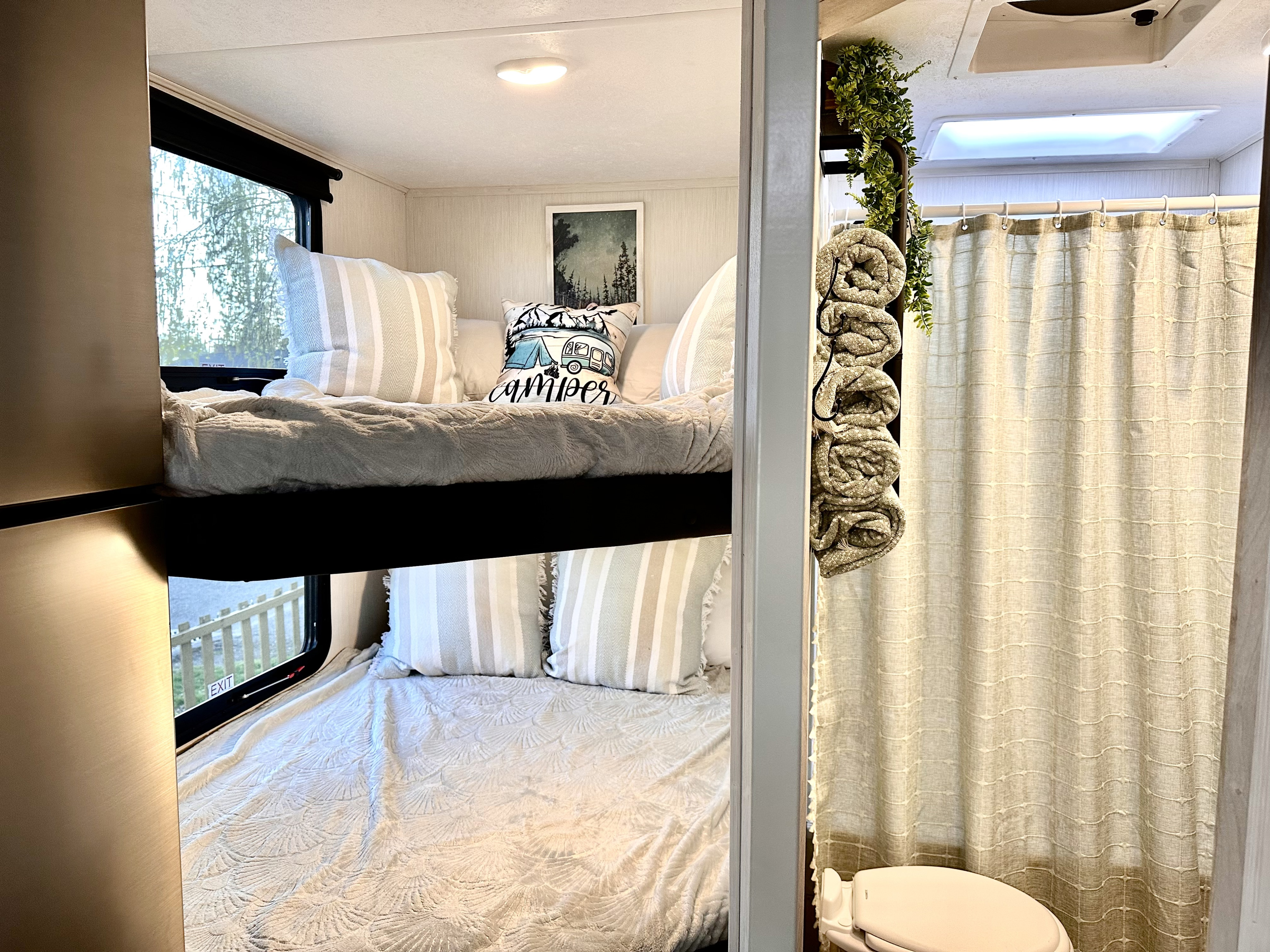 RV rental interior featuring cozy bunk beds with striped pillows and an adjacent compact bathroom with shower.. Forest River Wildcat 2023