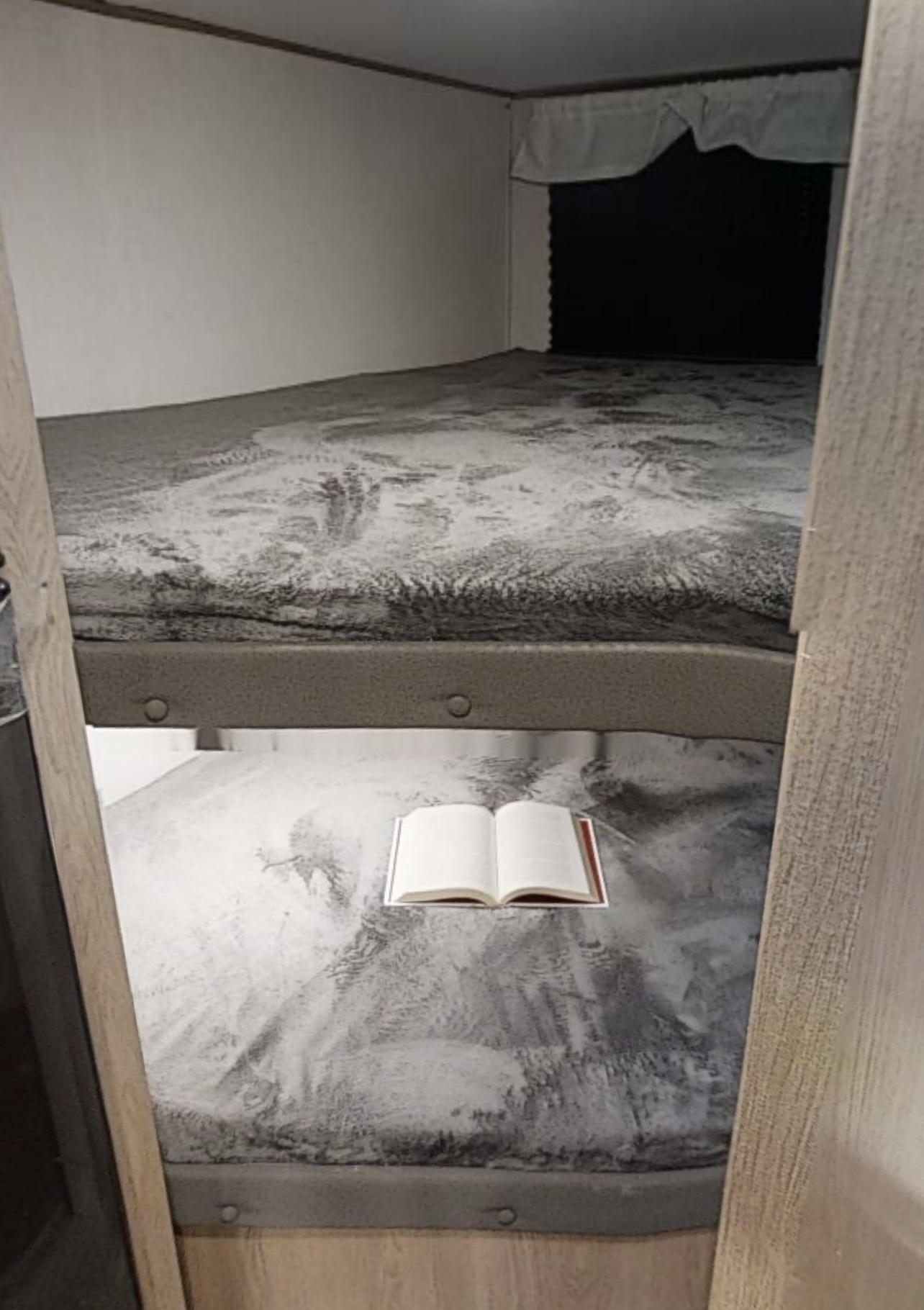 Cozy RV rental bunk beds with an open book, perfect for reading in this compact sleeping area.. Avenger Avenger Trailer 2022