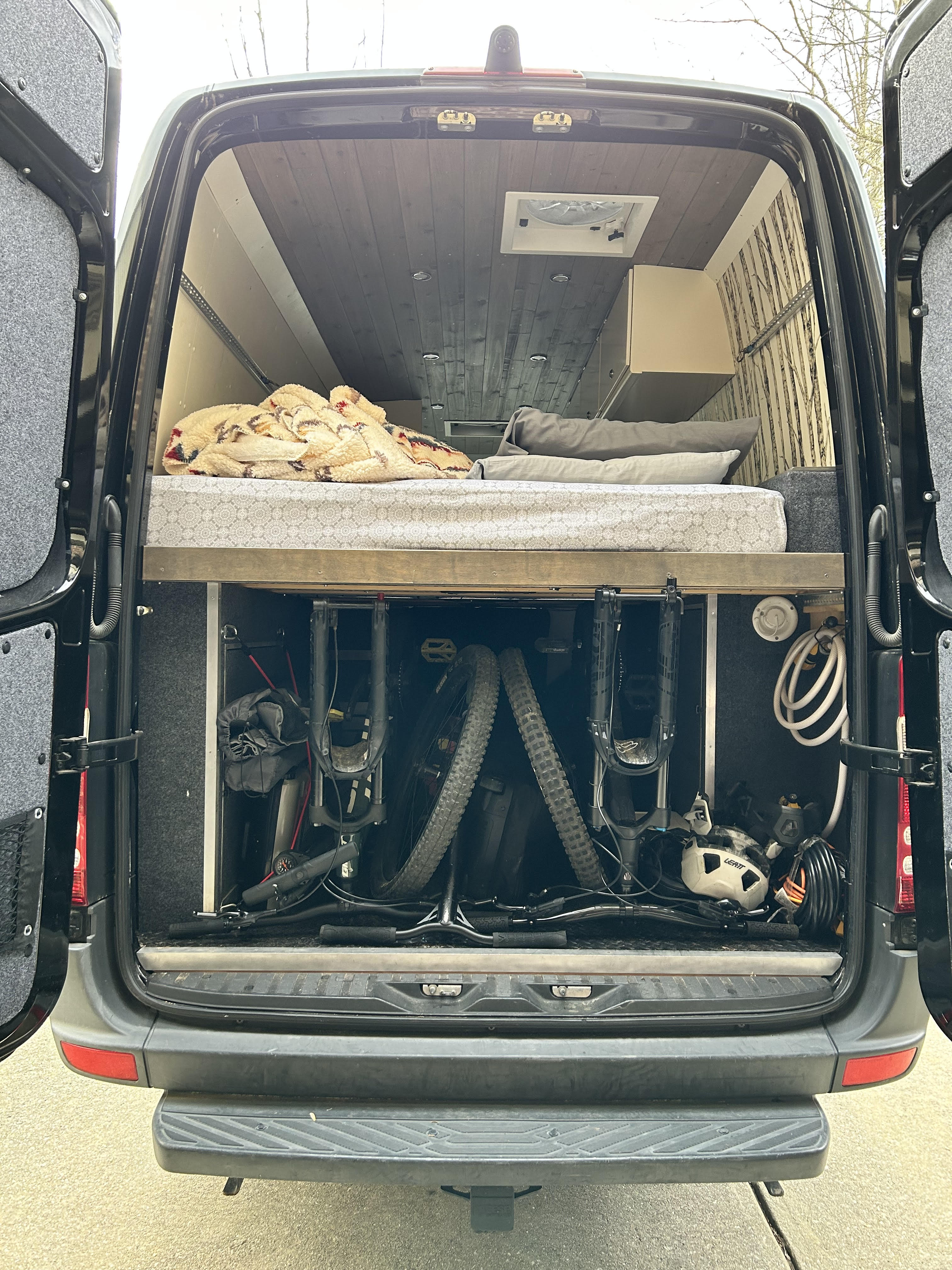 Rear view of a spacious custom RV rental camper van, revealing a comfortable bed above organized mountain bike storage.. Mercedes Sprinter 2012